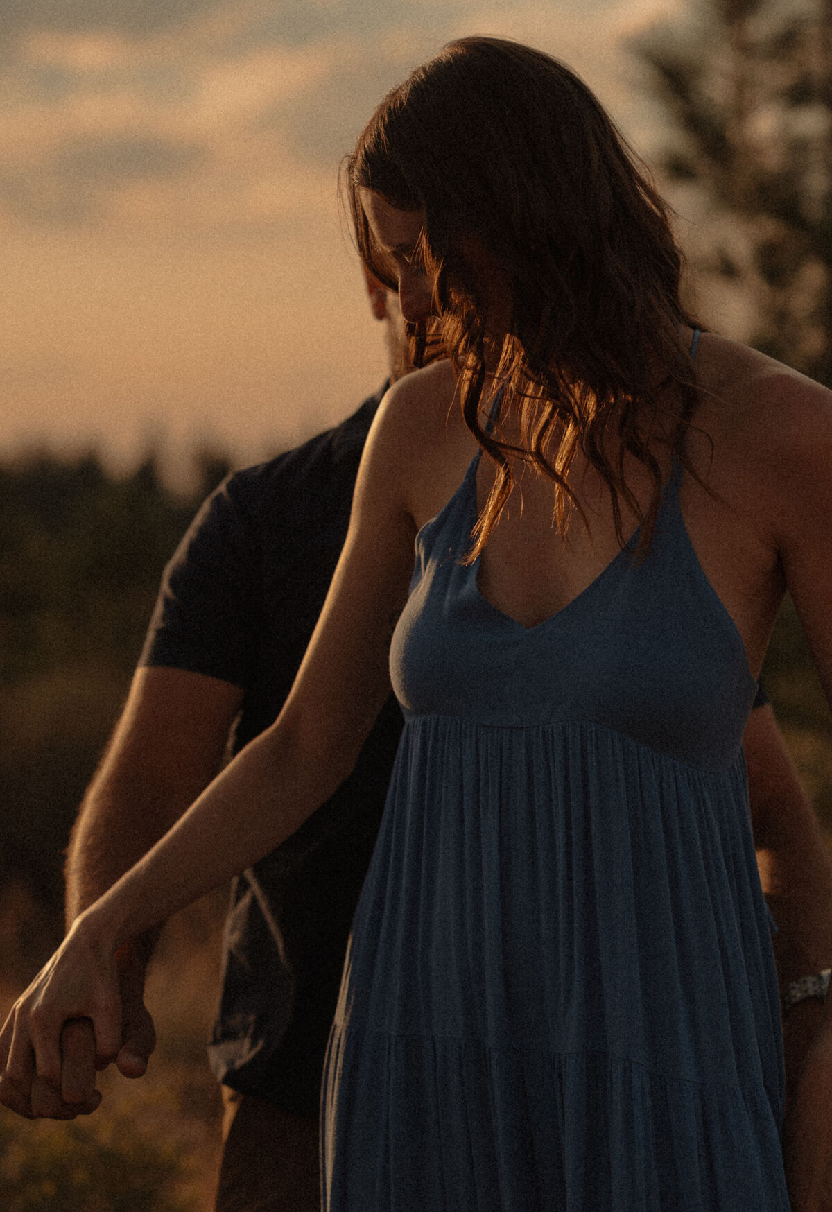 expecting parents hold hands and walk along nature during sunset in Bend, Oregon