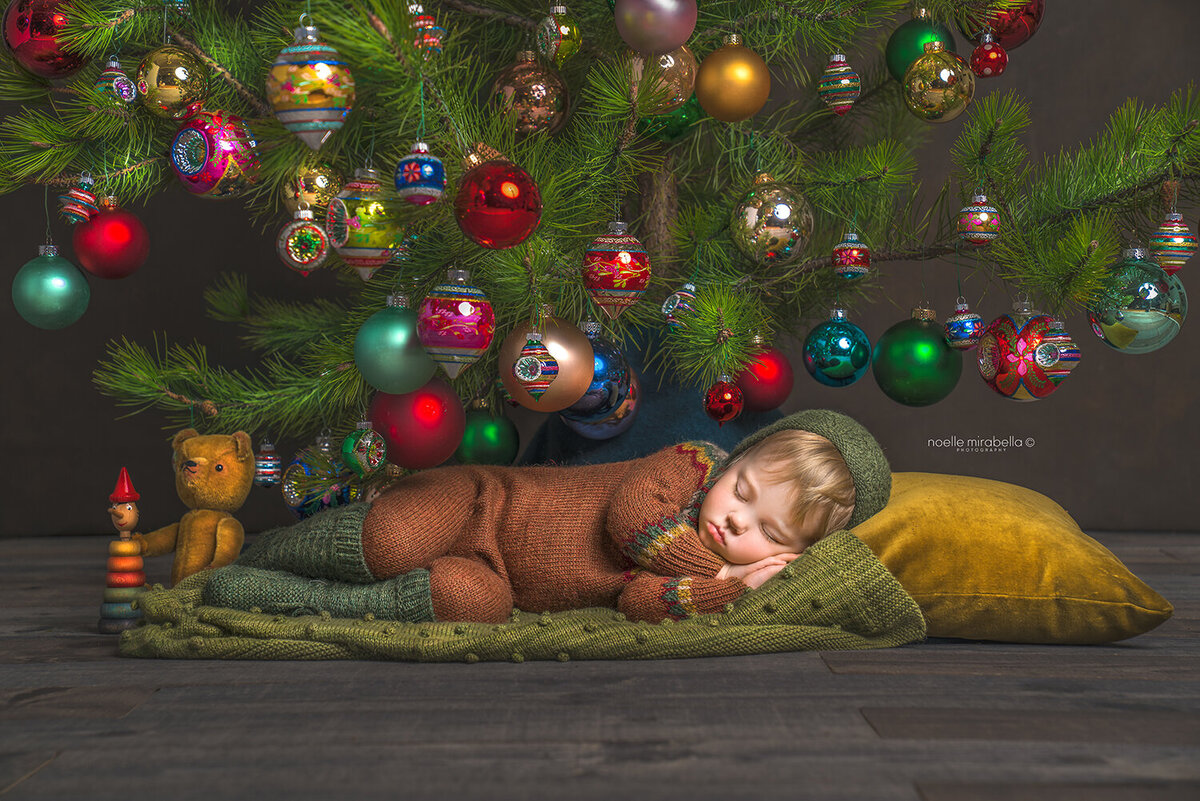Toddler wear knits sleeping under Christmas tree with vintage ornaments.