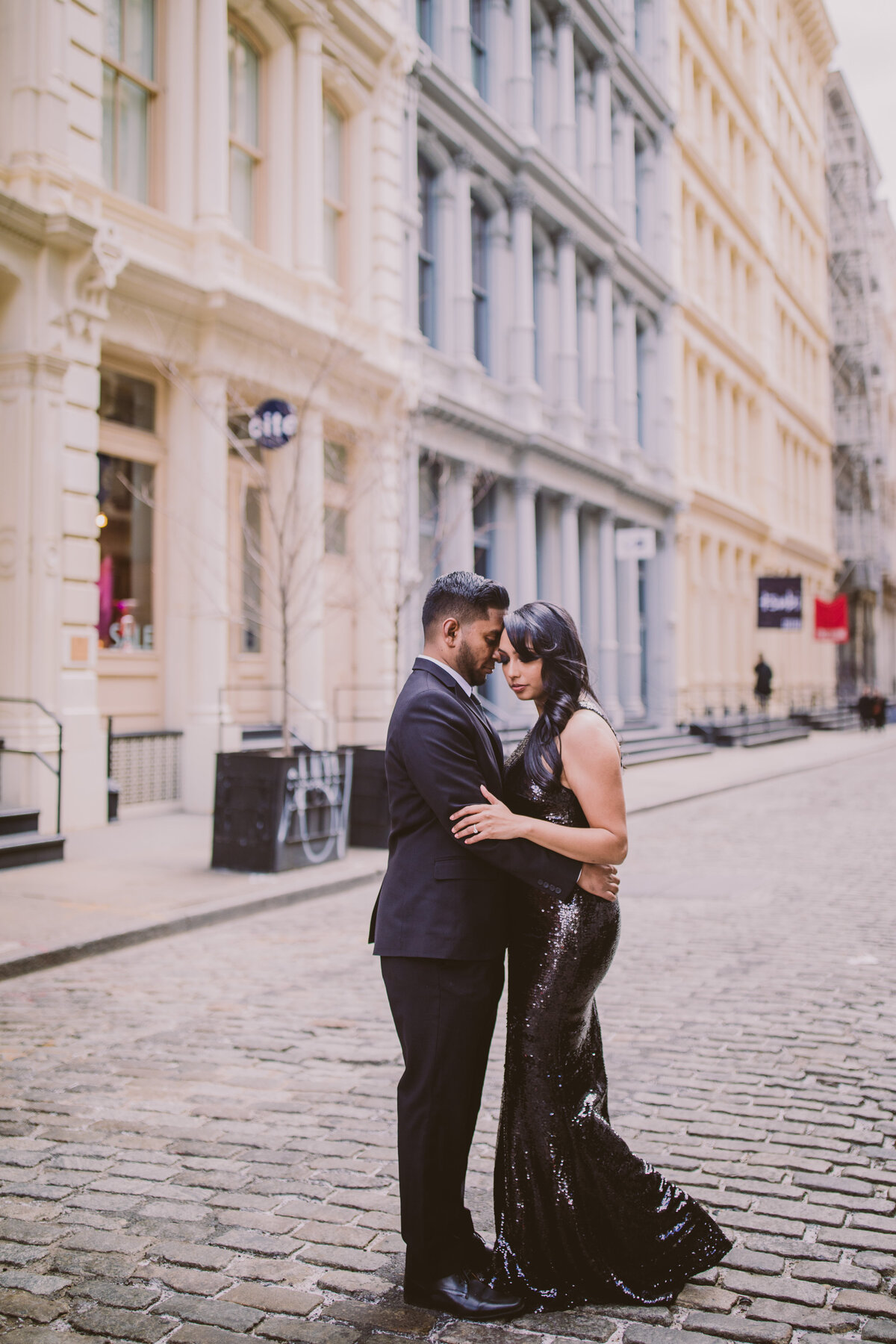 An engaged couple wearing formal black clothing share a moment on the cobblestone street in soho in new york city