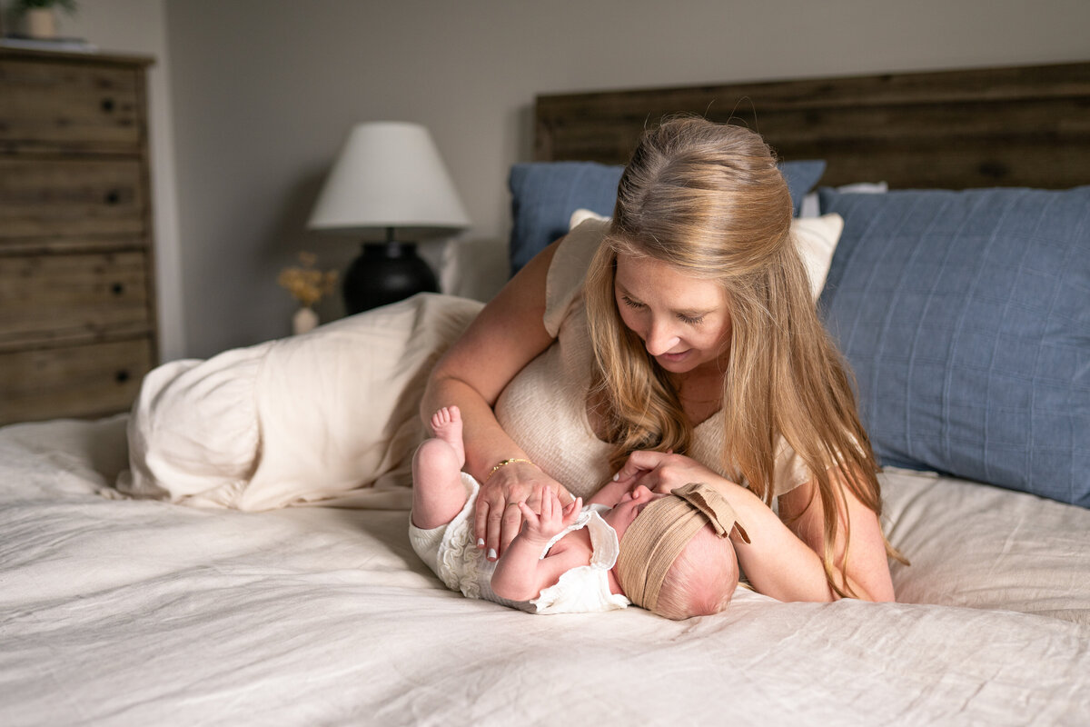 mom lying on bed with newborn baby rubbing her babies belly