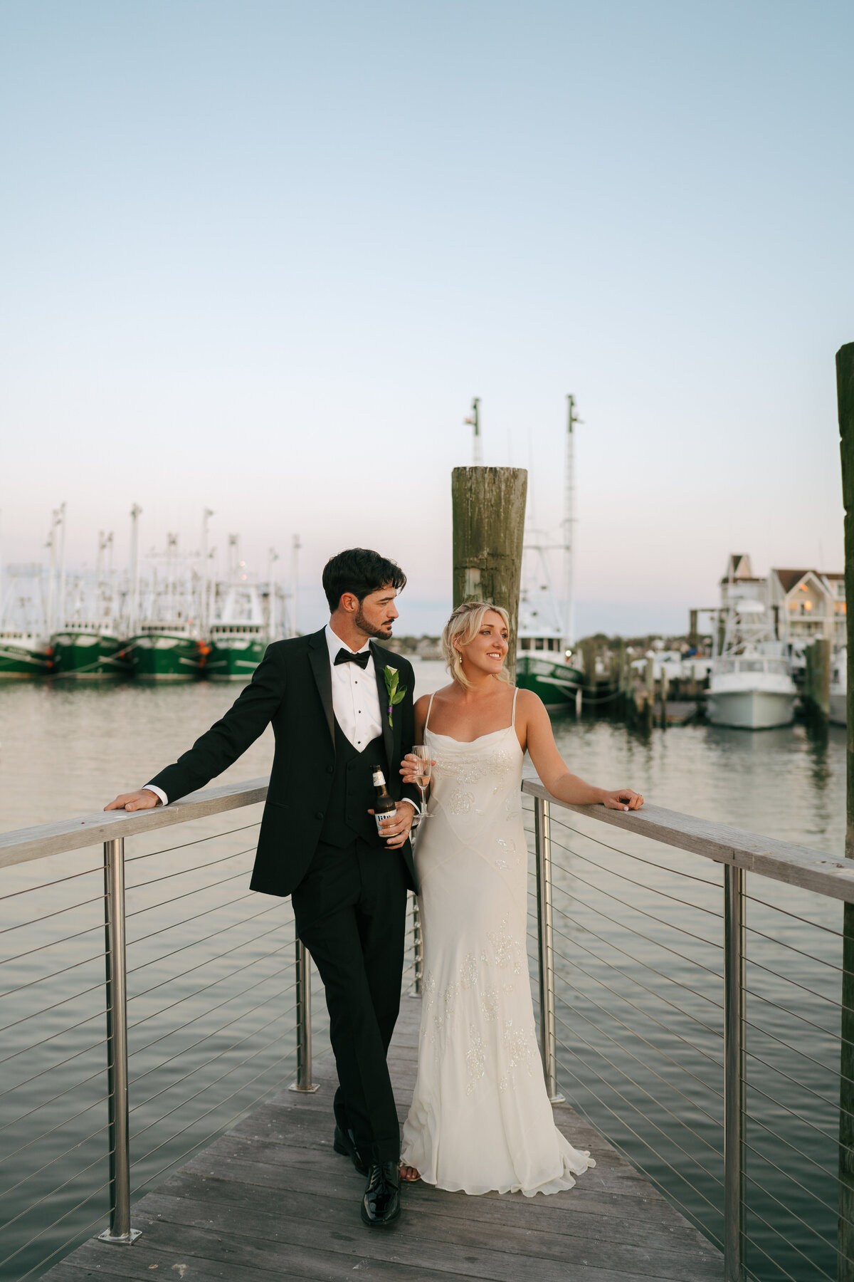 A bride and groom outside of their New Jersey wedding locking arms in front of an inlet filled with sailboats.