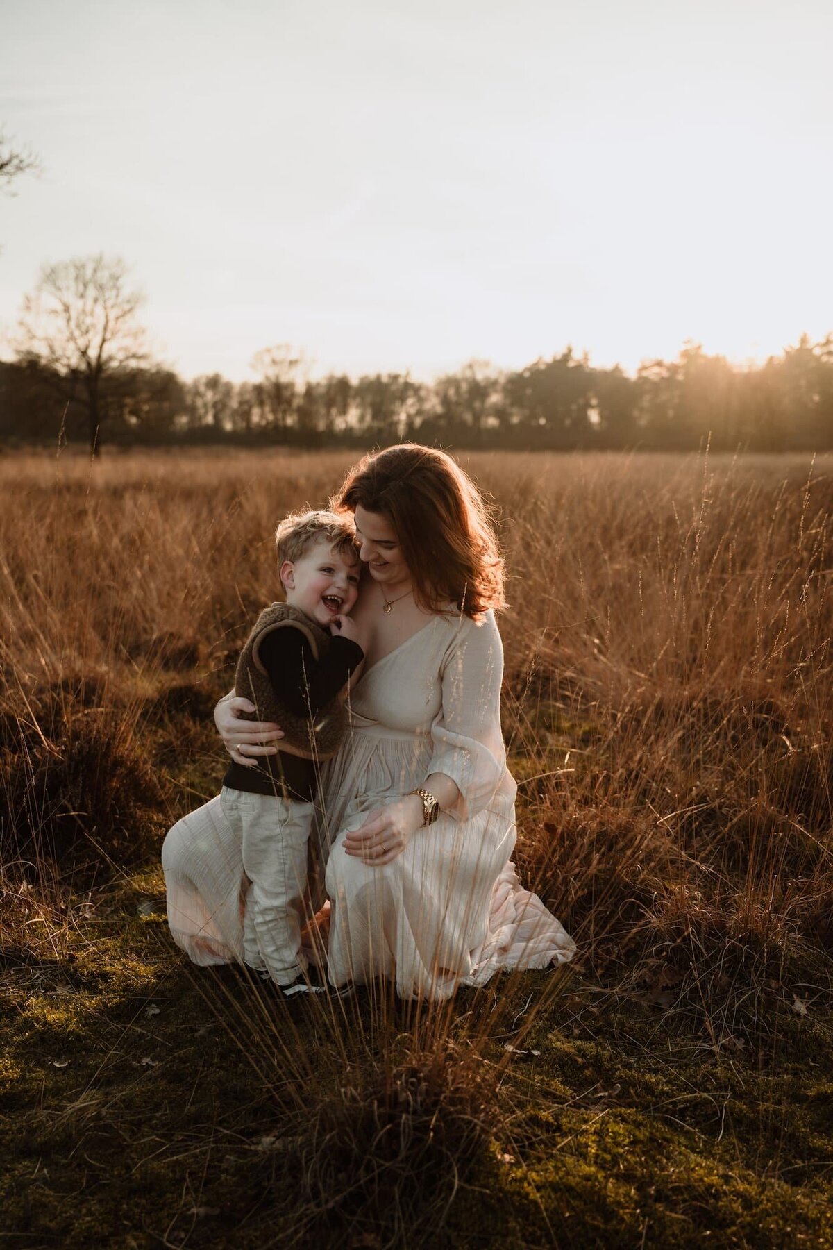 zwangere moeder met kindje in hoog gras tijdens golden hour door fotograaf Eline Hemelt