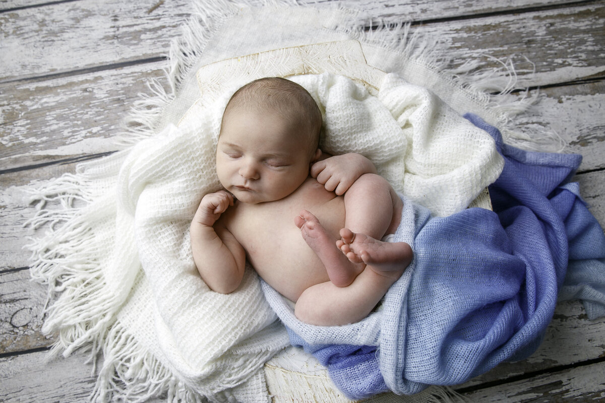 Tiny newborn baby lying on a white blanket with blue blanket for color