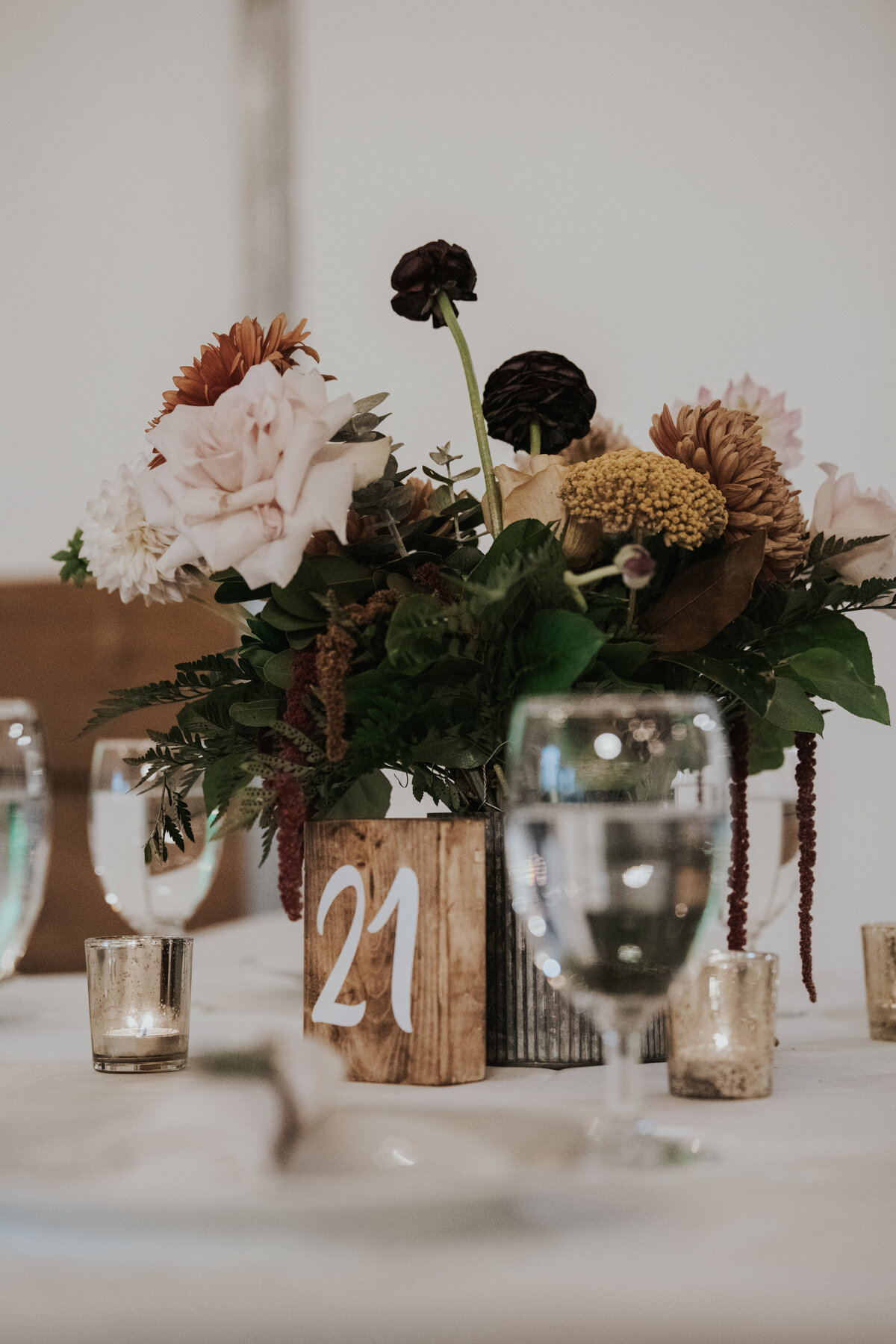 Fall colored wedding reception centerpiece with pink, burgundy, orange, and yellow flowers with a wooden table number.