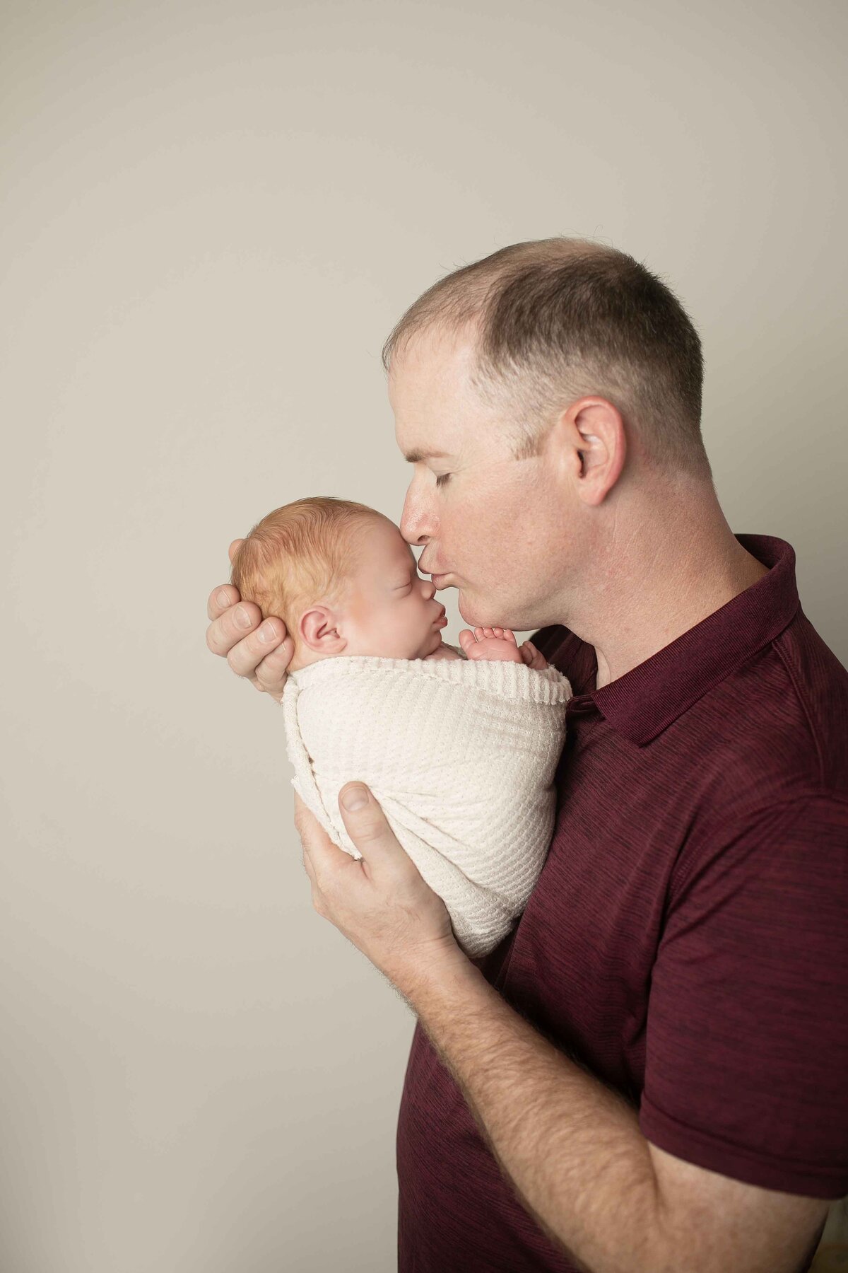 Dad posing with his newborn, supporting his tiny baby in his arms with care