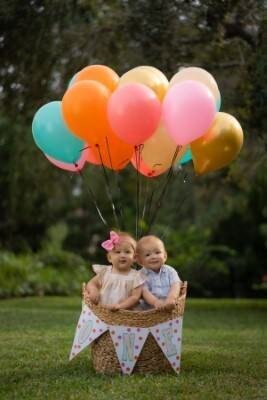 Two young children sitting in wicker basket holding colorful balloons during outdoor family photo session by St Augustine family photographers
