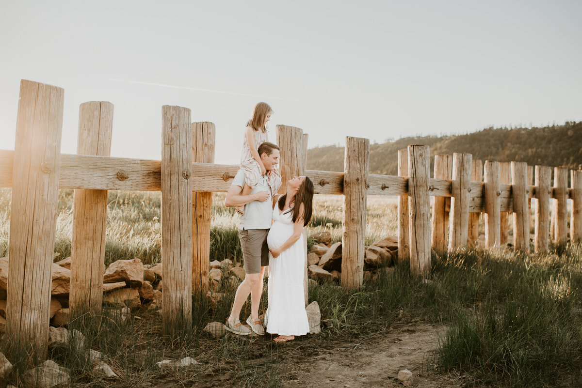 family with girl on dads shoulders and mom holding pregnant belly