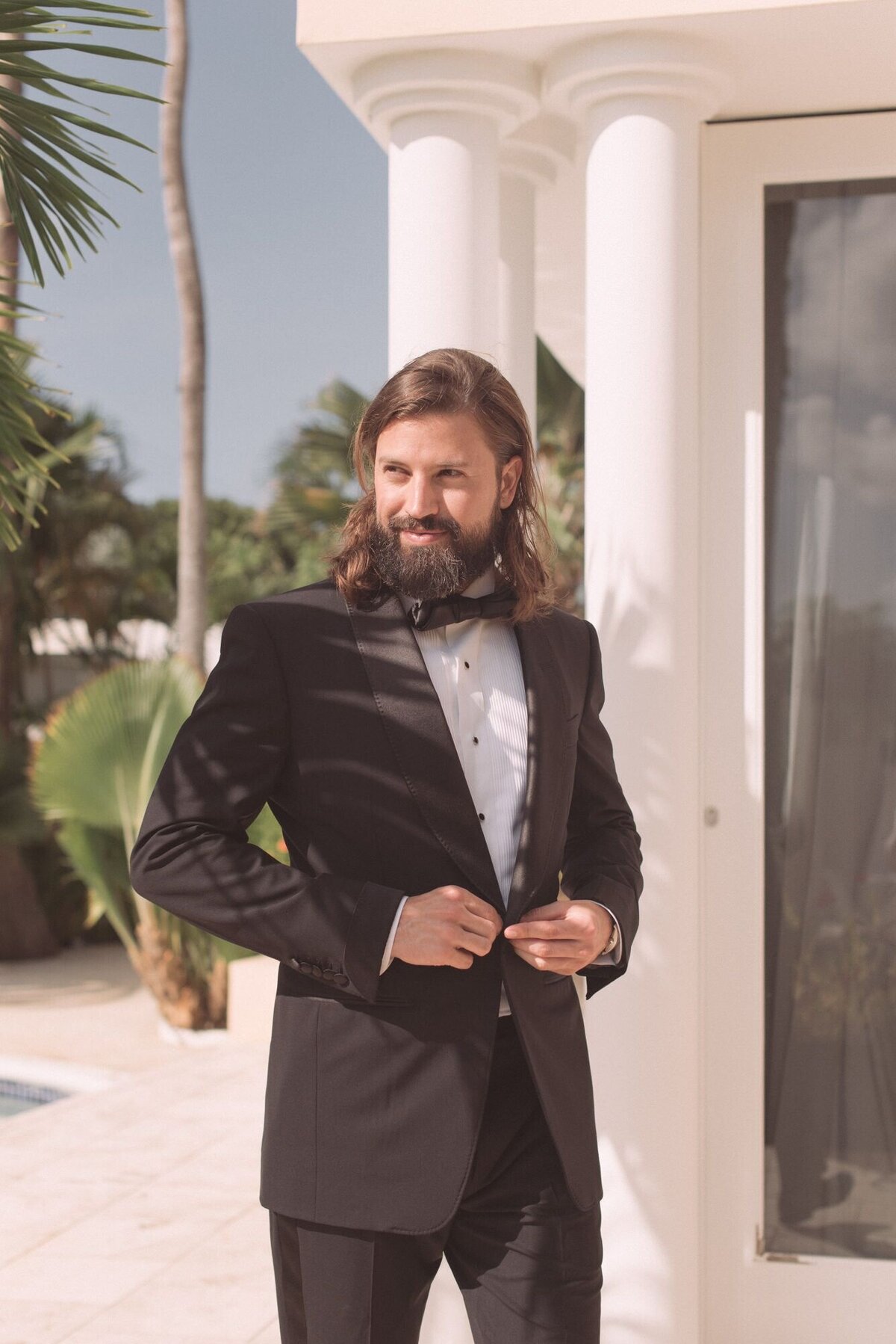 groom  with long hair buttoning tom ford tux  before high end wedding ceremony in orajenstad aruba.