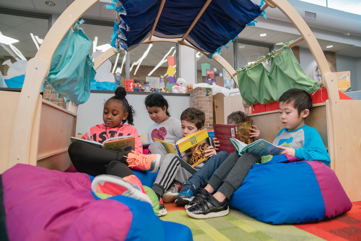 Five young students reading in a colorful reading tent in their classroom