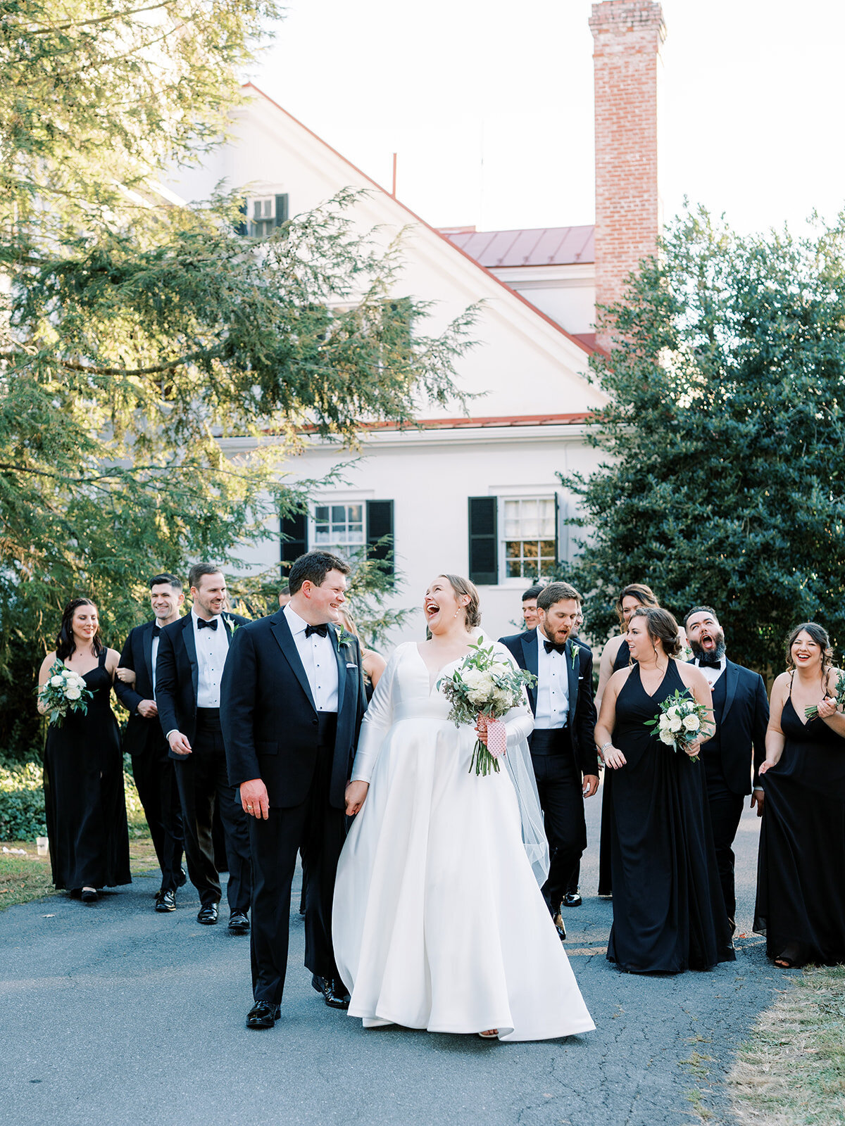 Bride and groom laugh as they walk with their bridal party at rosemont manor