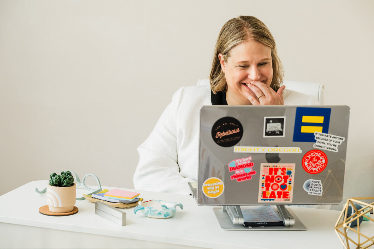 Mya Andersen sits at a desk, looking at a laptop covered in colorful stickers—she’s excited about helping students Get College-Ready This Summer with The Summer Jumpstart Program