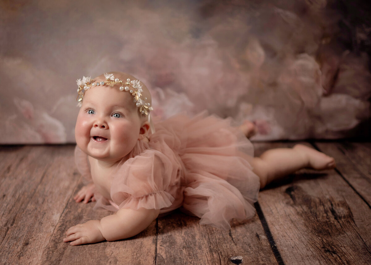 A baby girl smiles big for her Pella Family Photographer in her pink tutu