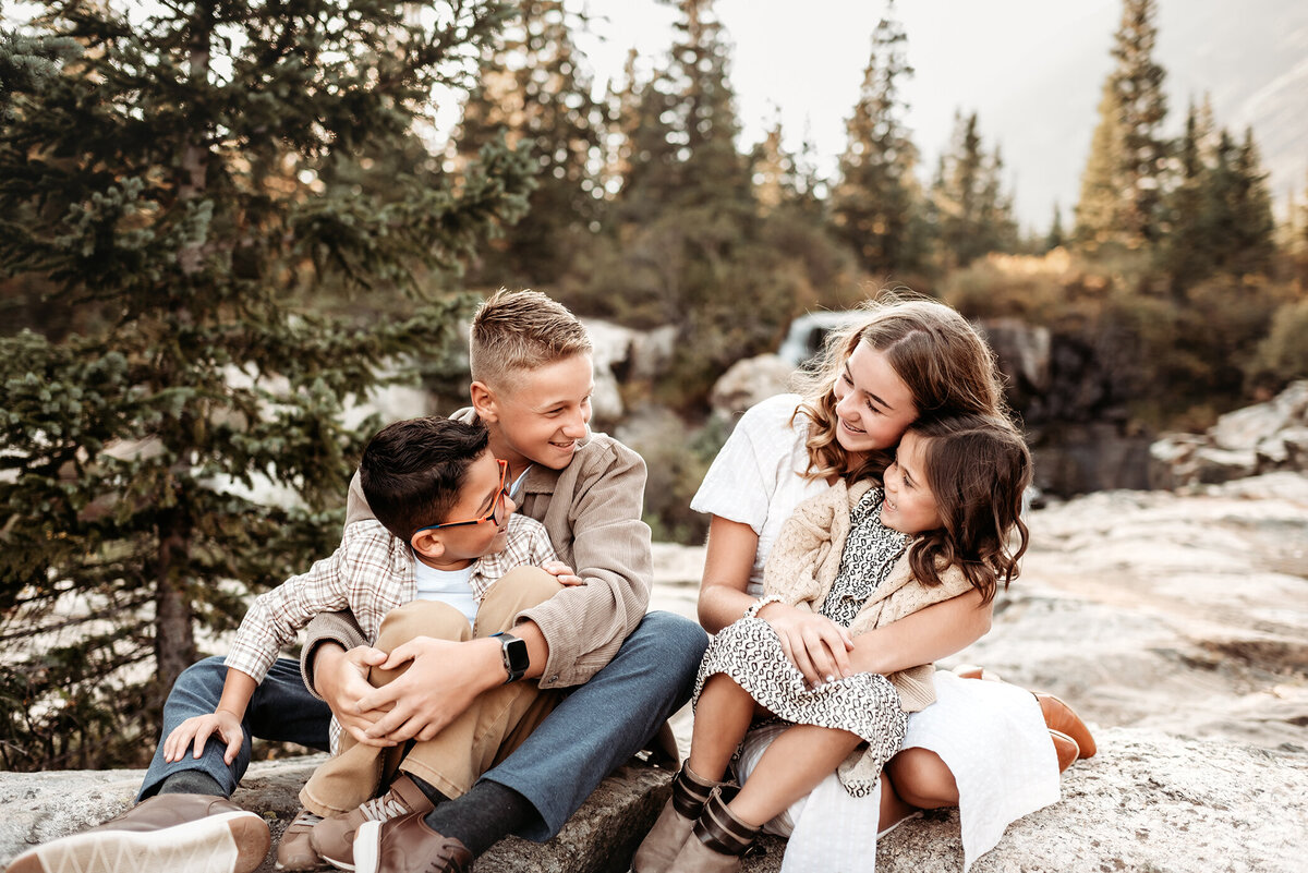 four siblings in the mountain forest sitting and looking at each other on rocks