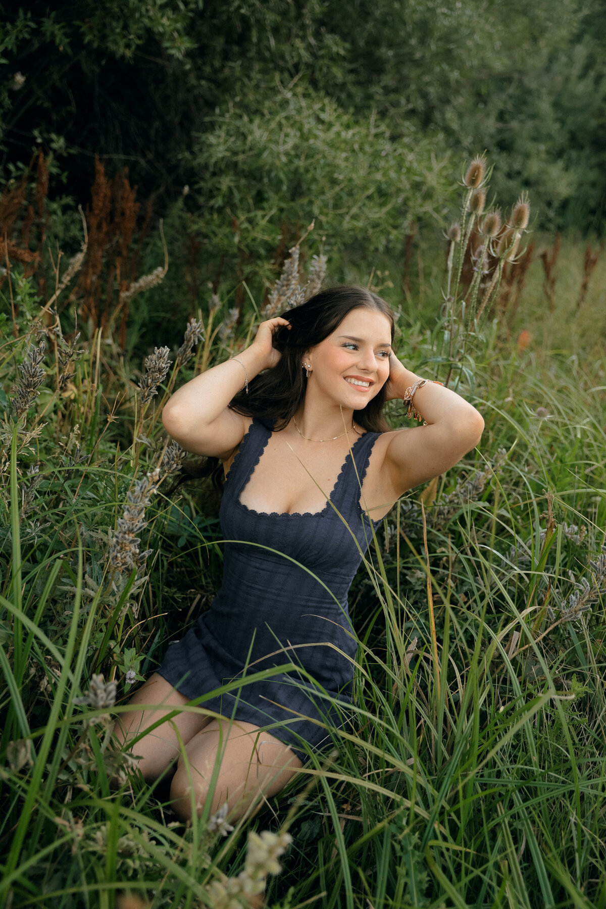 Sun-Drenched Senior Portrait of Girl Twirling in Field with Golden Light Flaring Through Trees