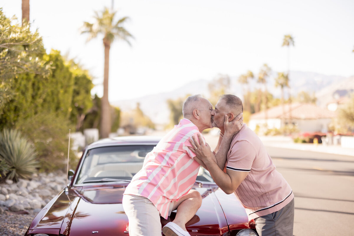One partner lifts the other in a joyful embrace under palm trees, framed by blue skies and desert warmth.