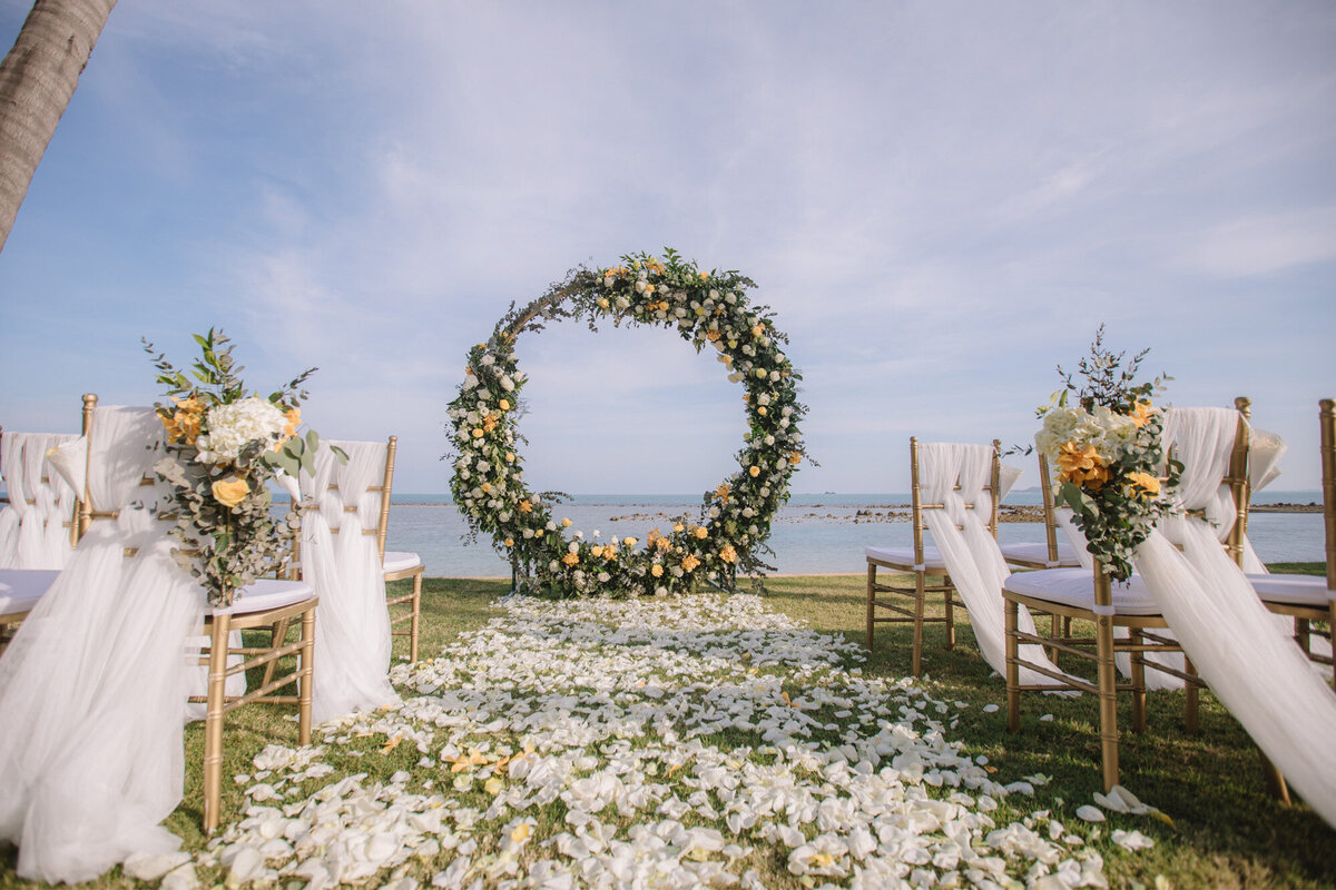 Wedding ceremony site at the seaside with round florals backdrop and floral petals on the aisle