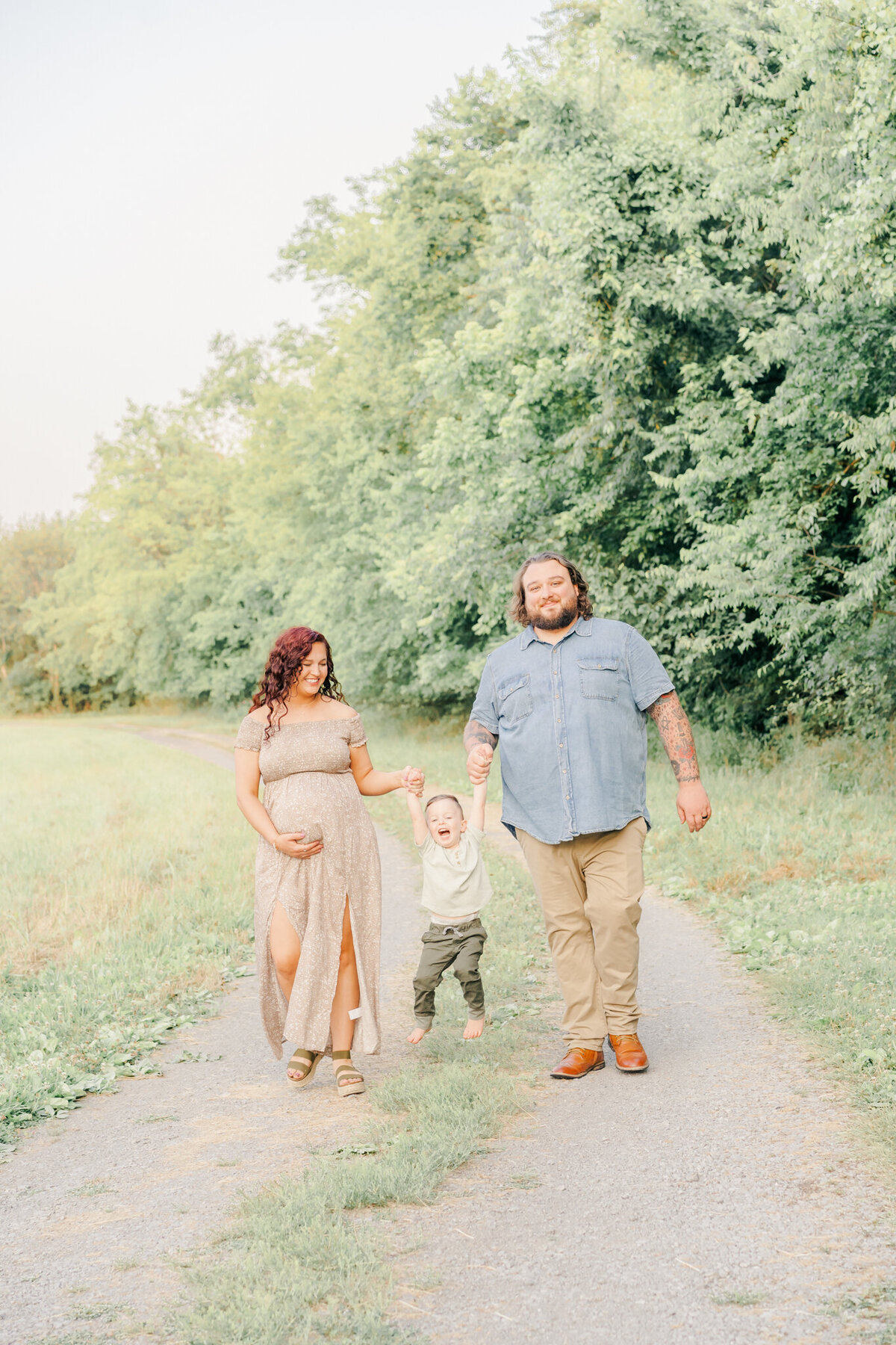 mom and dad with toddler walking down path swinging the laughing toddler