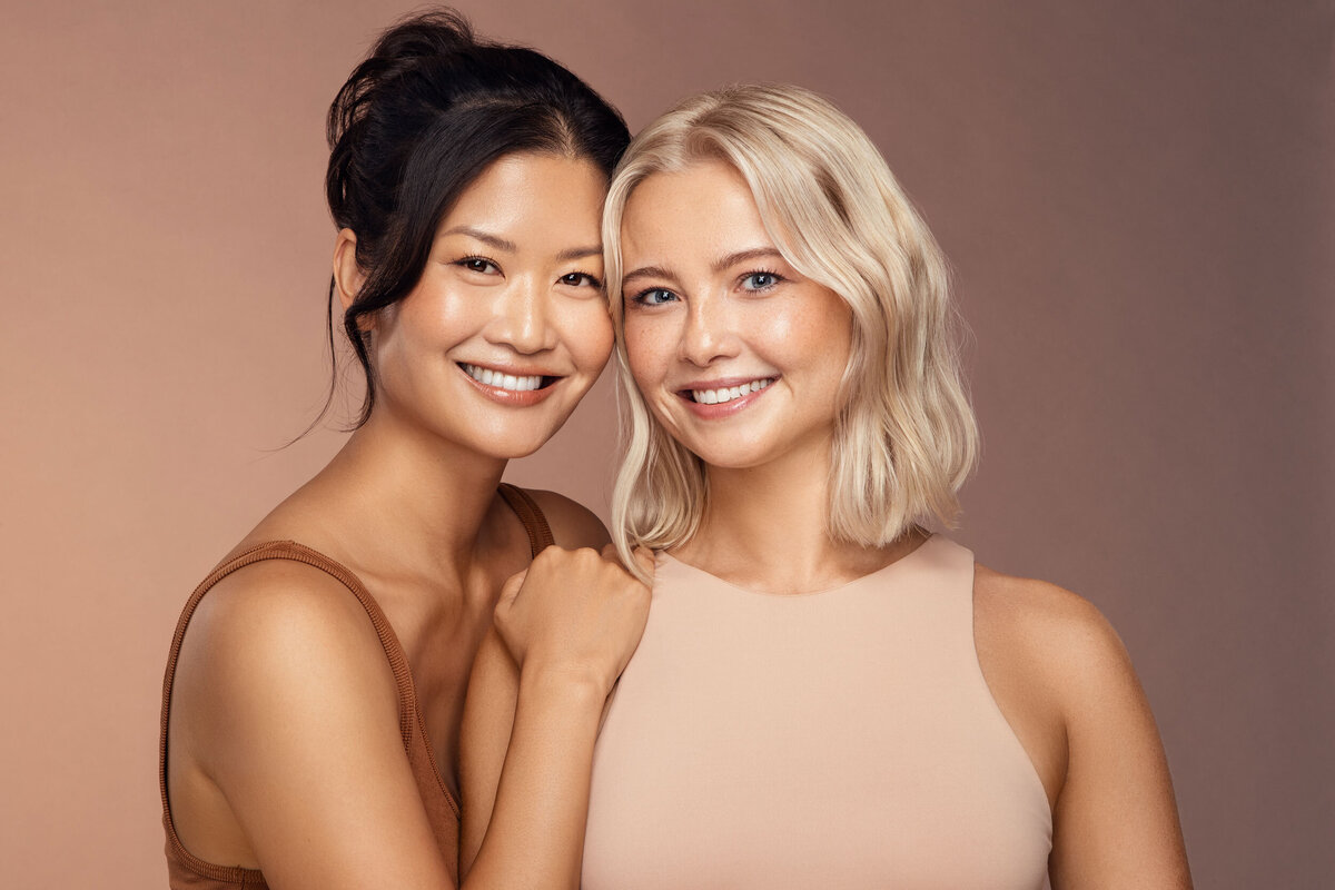 Danielle Yu and Paulina Michaels smiling together in a soft-lit studio portrait, showcasing their natural beauty and radiant expressions, captured by Ylva Erevall.