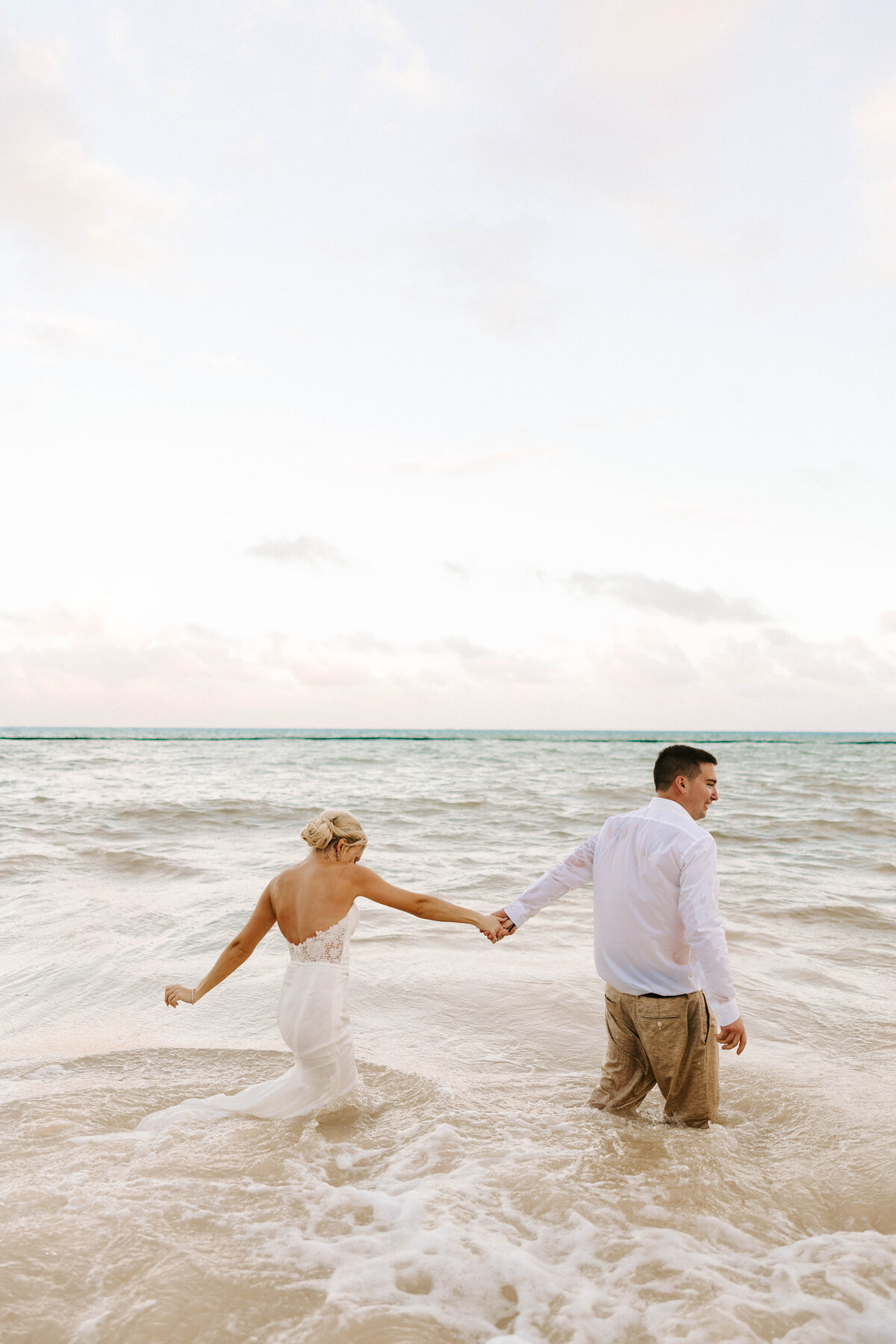 Groom, leading his bride into the ocean during adventure photo shoot. Beachside wedding Cancun, Mexico