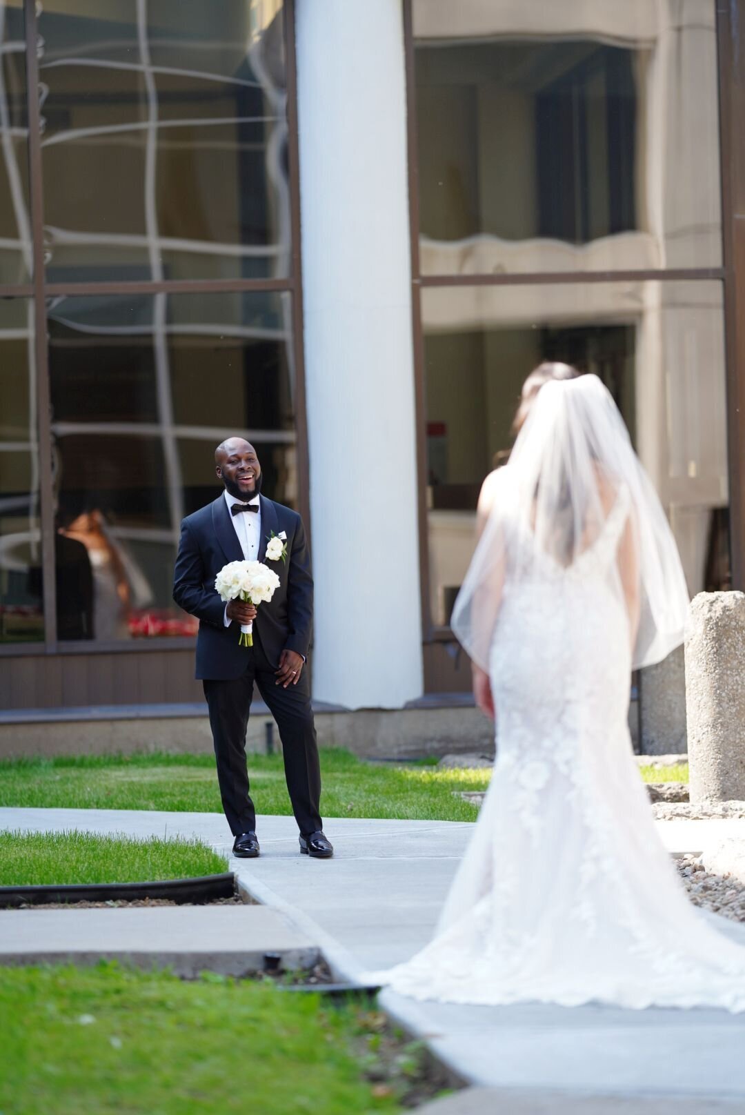 A captivating shot from behind the bride, showing the groom standing in front of her, holding a bouquet and gazing at her with love and admiration. The image beautifully captures the anticipation and connection between the couple on their wedding day.