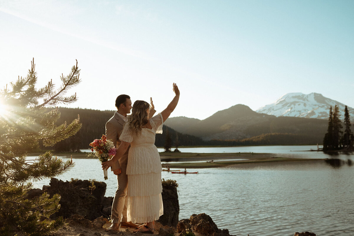 bride and groom standing next to Sparks Lake wave to friends and family after their private ceremony