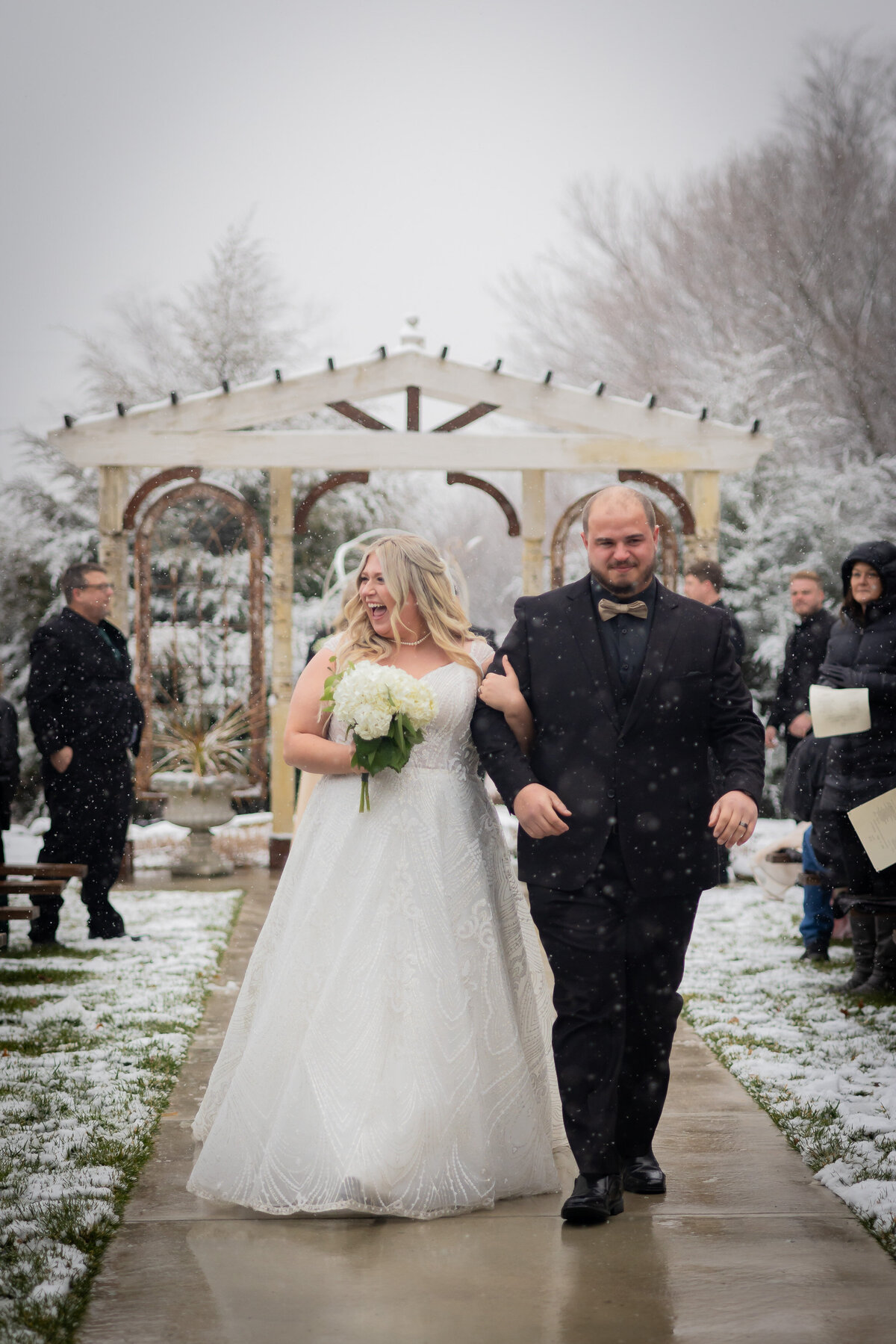 bride and groom leaving the outside snowy ceremony and smiling at guests
