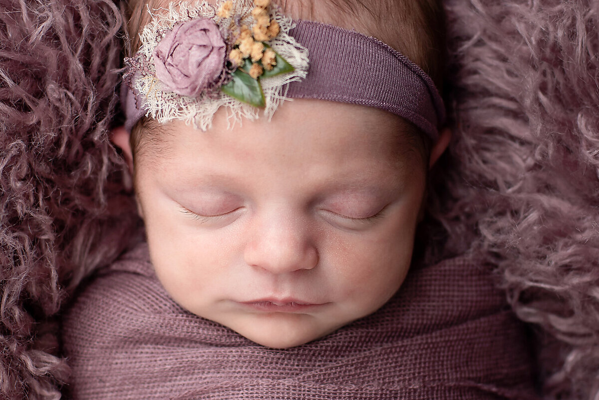 Close up of a sleeping newborn girl wearing a purple wrap and matching headband.
