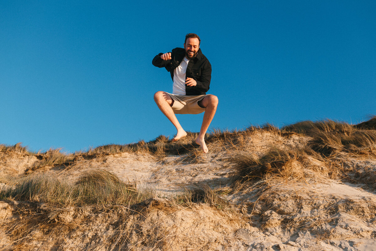 Man jumping off sand dunes photo with  blue sky 