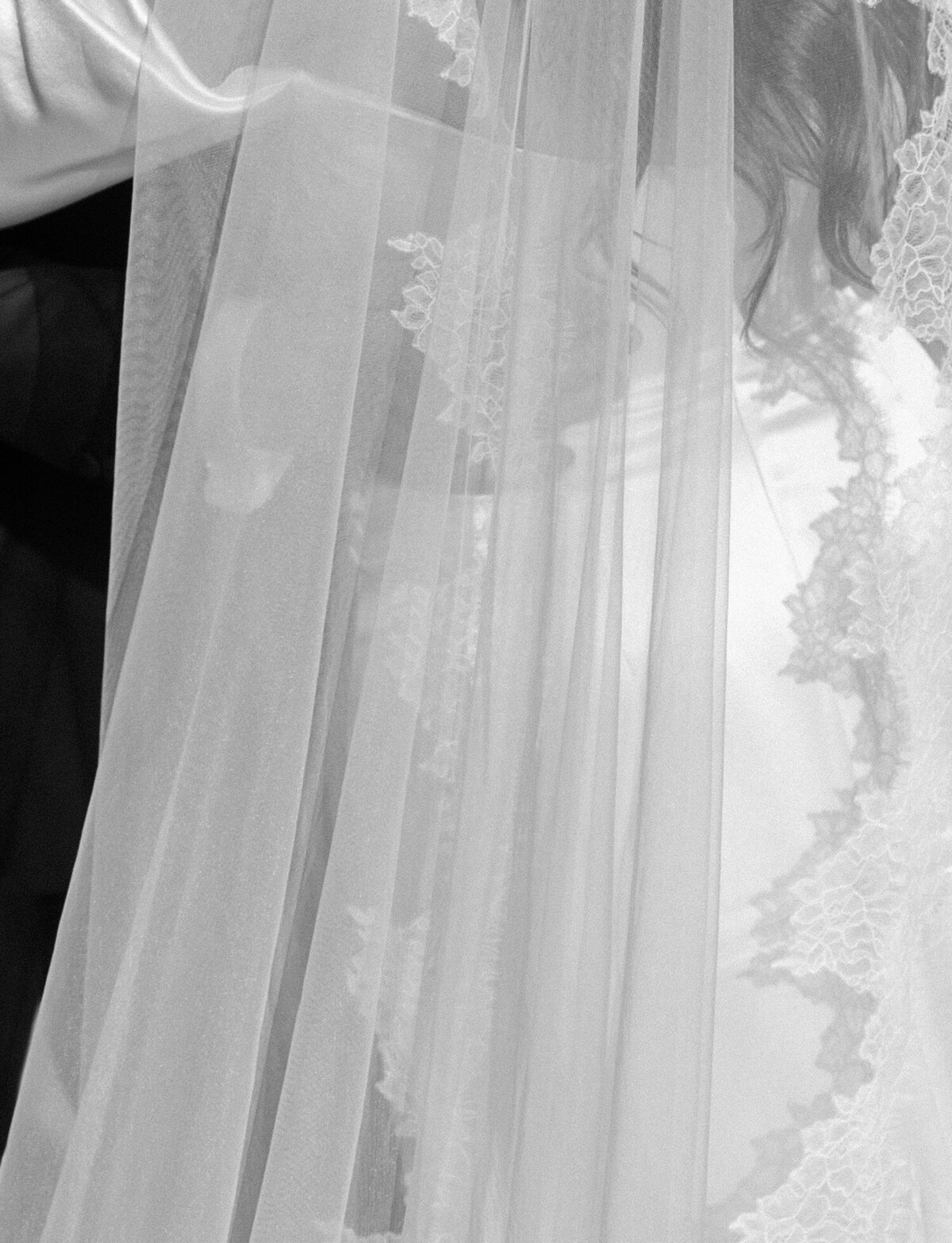 Soft black and white detail of groom embracing bride through long lace veil