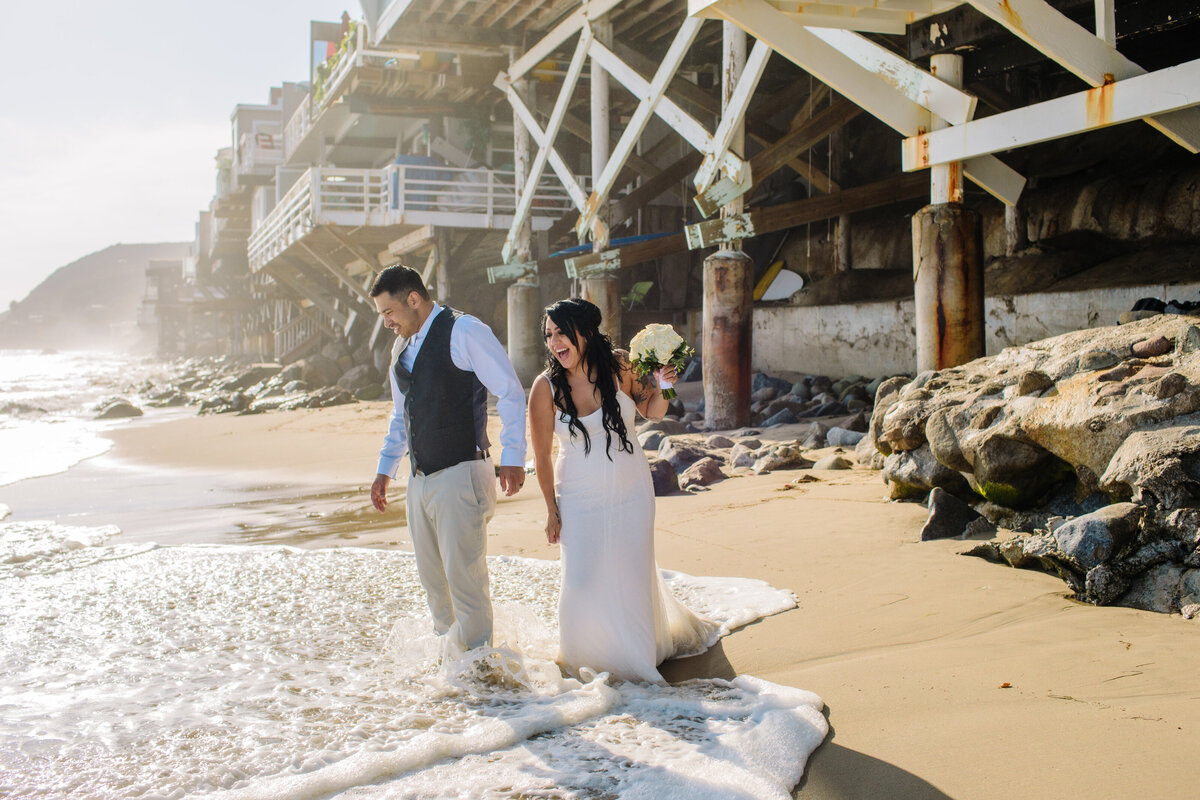 bride and groom get their feet wet in the ocean on the beach