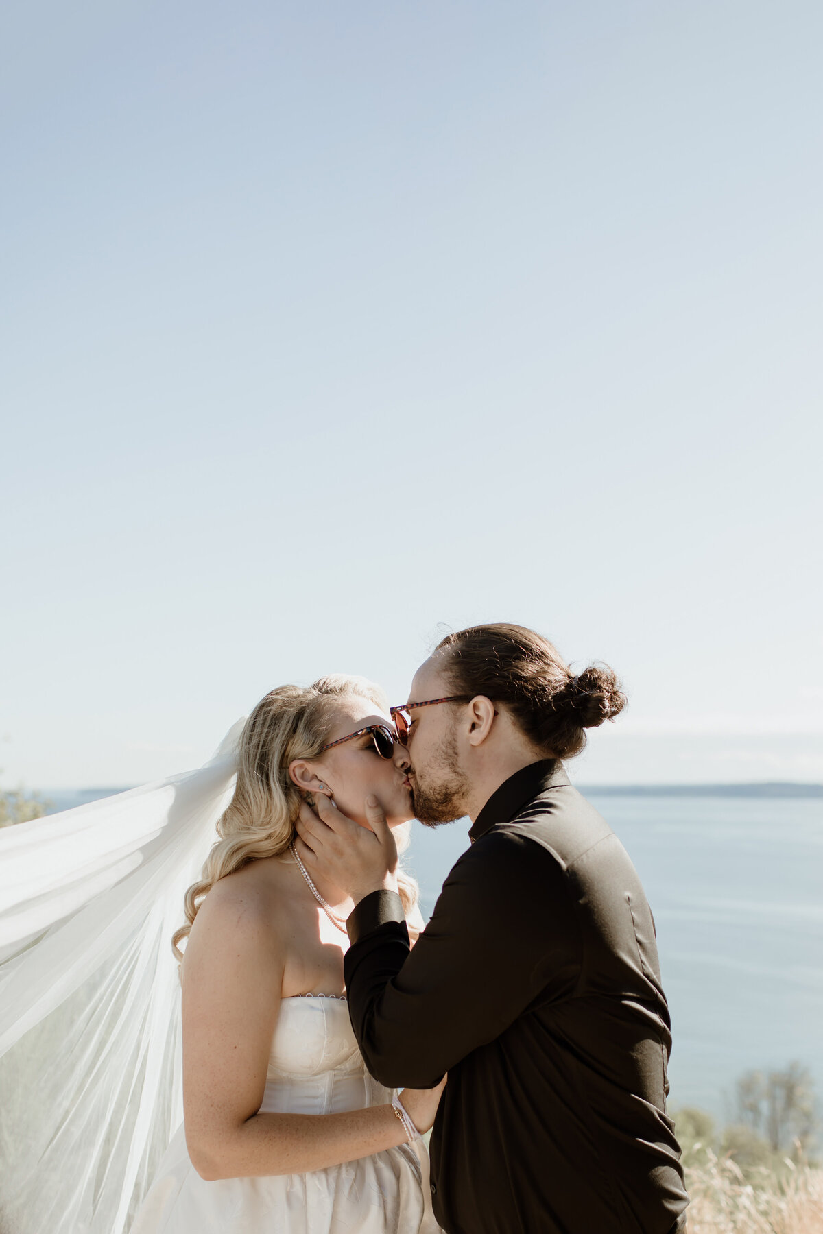 A romantic kiss between a bride in groom on the bluffs at Discovery Park in Seattle.  Captured by Fort Worth Wedding Photographer, Megan Christine Studio