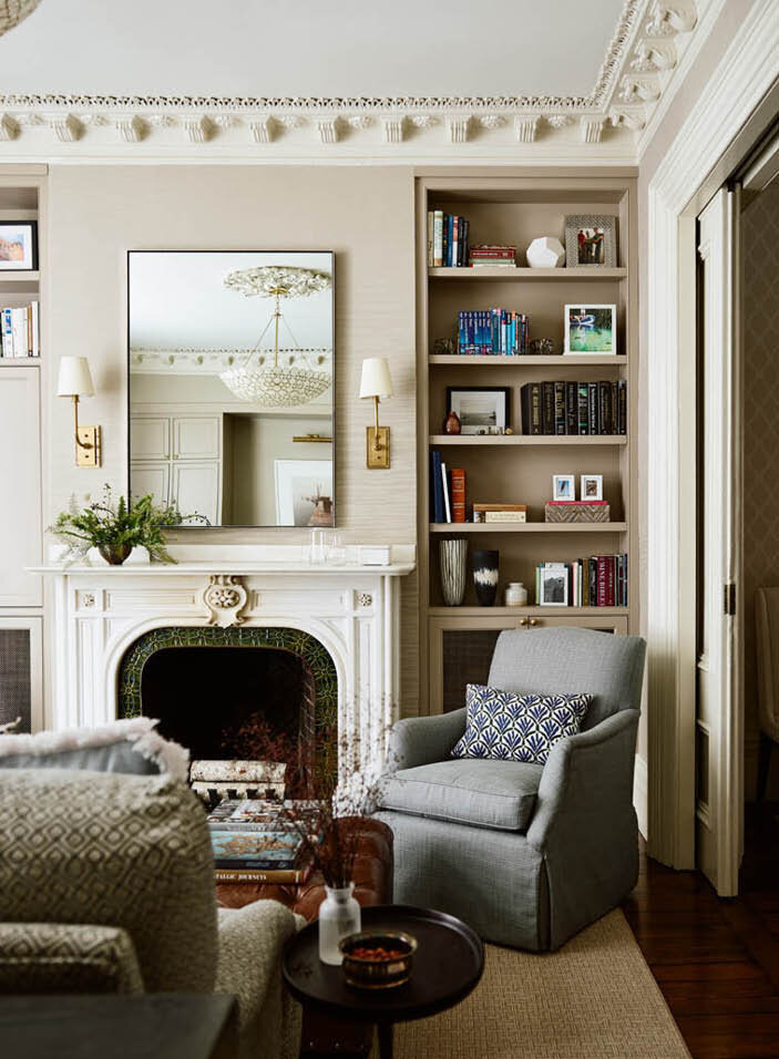 A working wood-burning fireplace with original marble and tile surround, custom shelving, brass sconces, and a simple mirror. Timeless design by Sarah Scales.