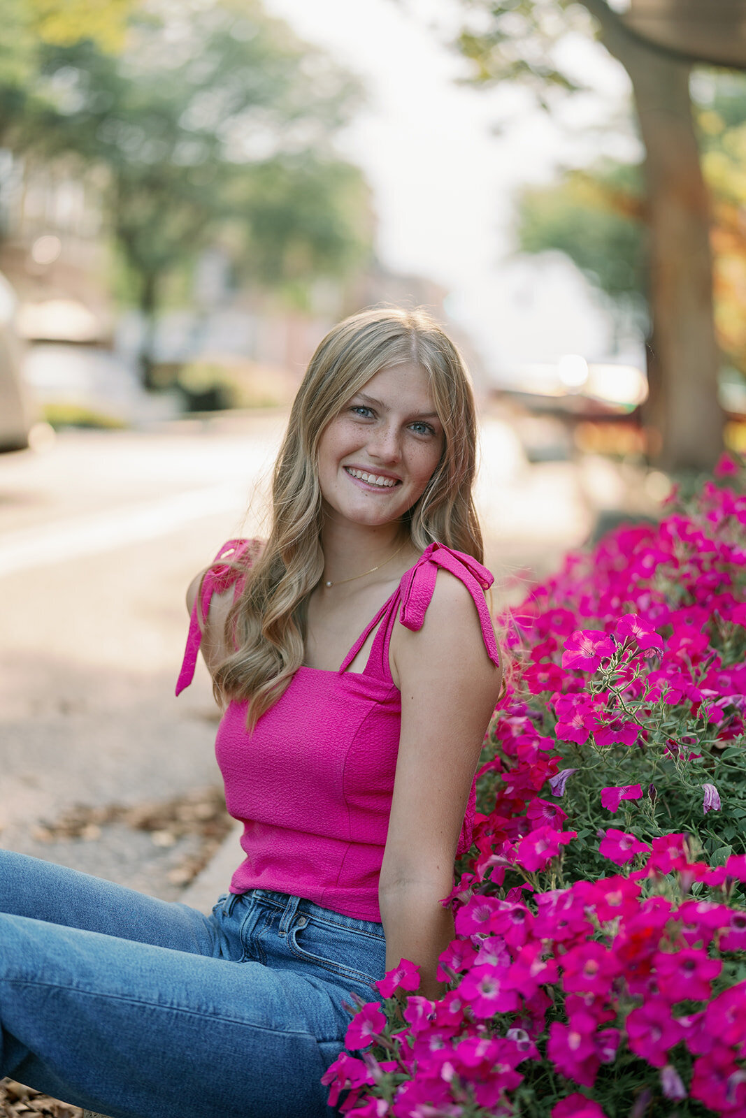 Senior girl sitting near bright pink flowers along 8th Street in downtown Holland, Michigan for her senior pictures.