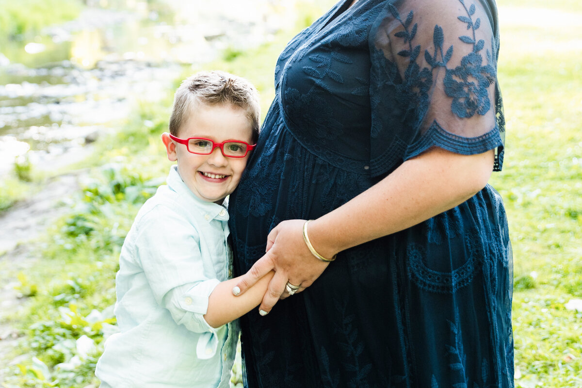 big brother smiles and holds mom's pregnant belly