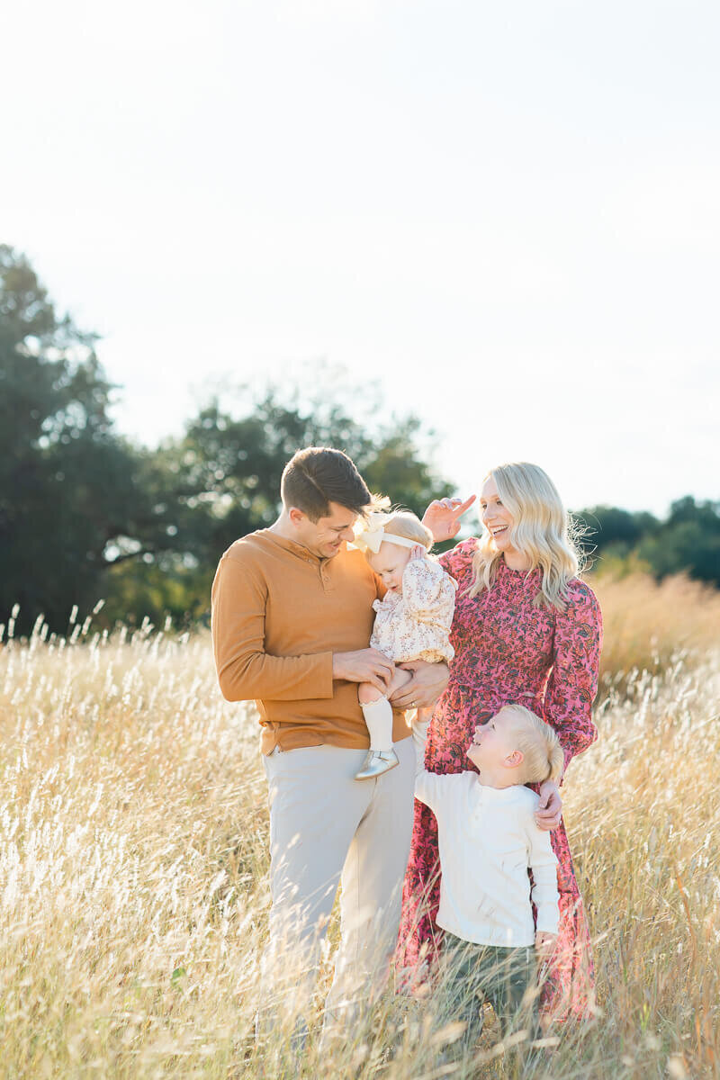 a mother, father, young son and daughter play together in a field while captured by an Austin Texas family photographer.