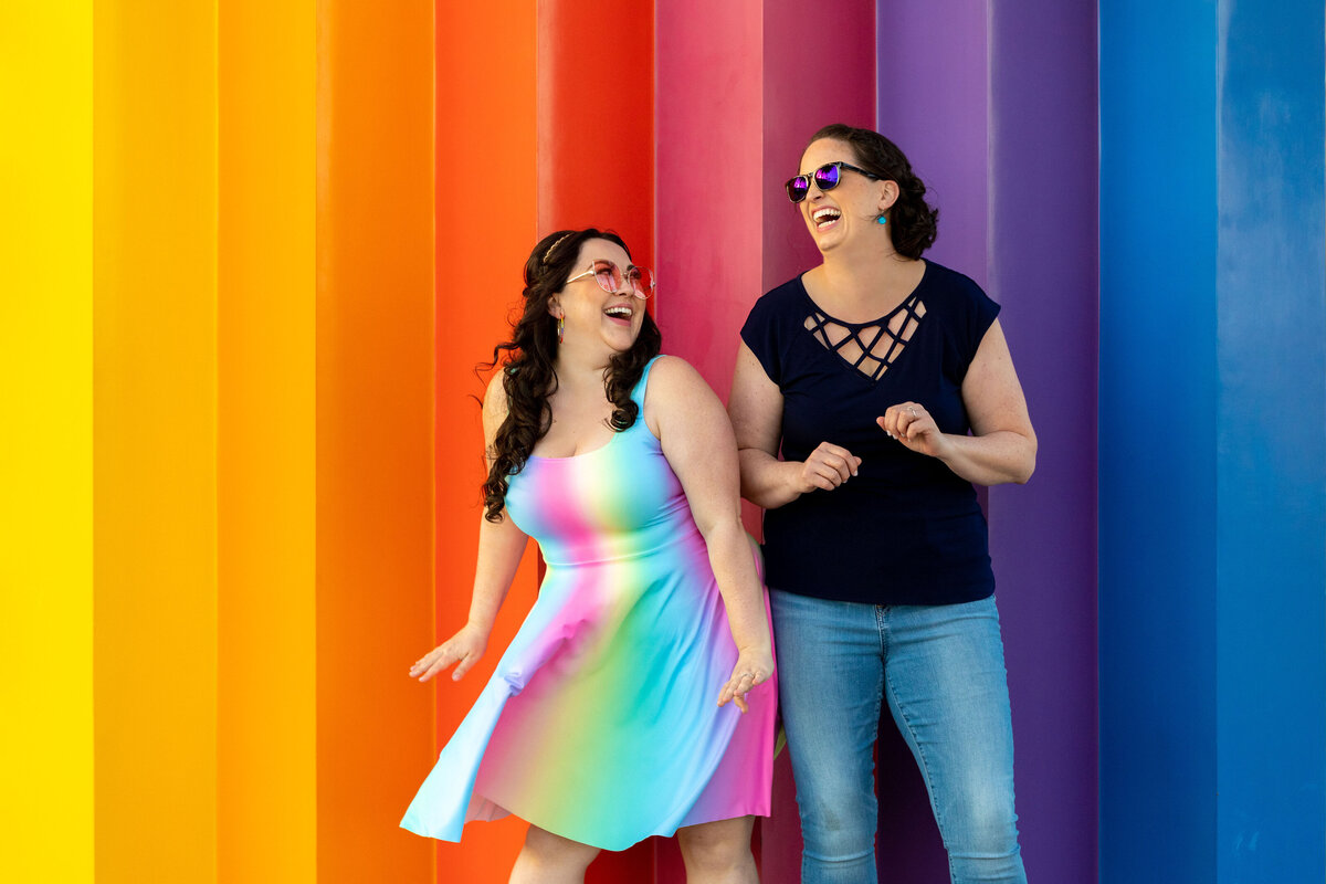 A couple dancing in front of a rainbow wall.