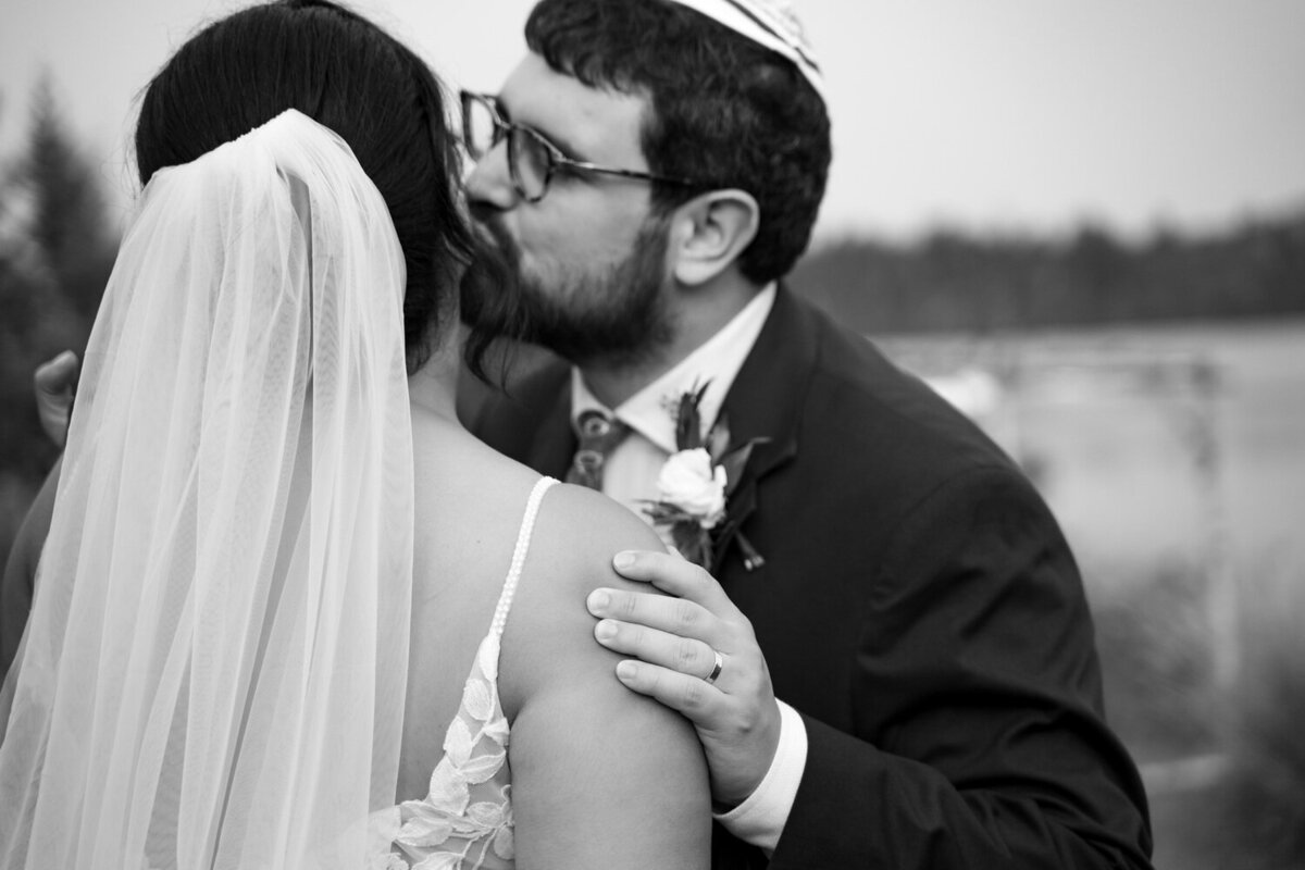 black and white image of a Jewish groom kissing the cheek of his bride