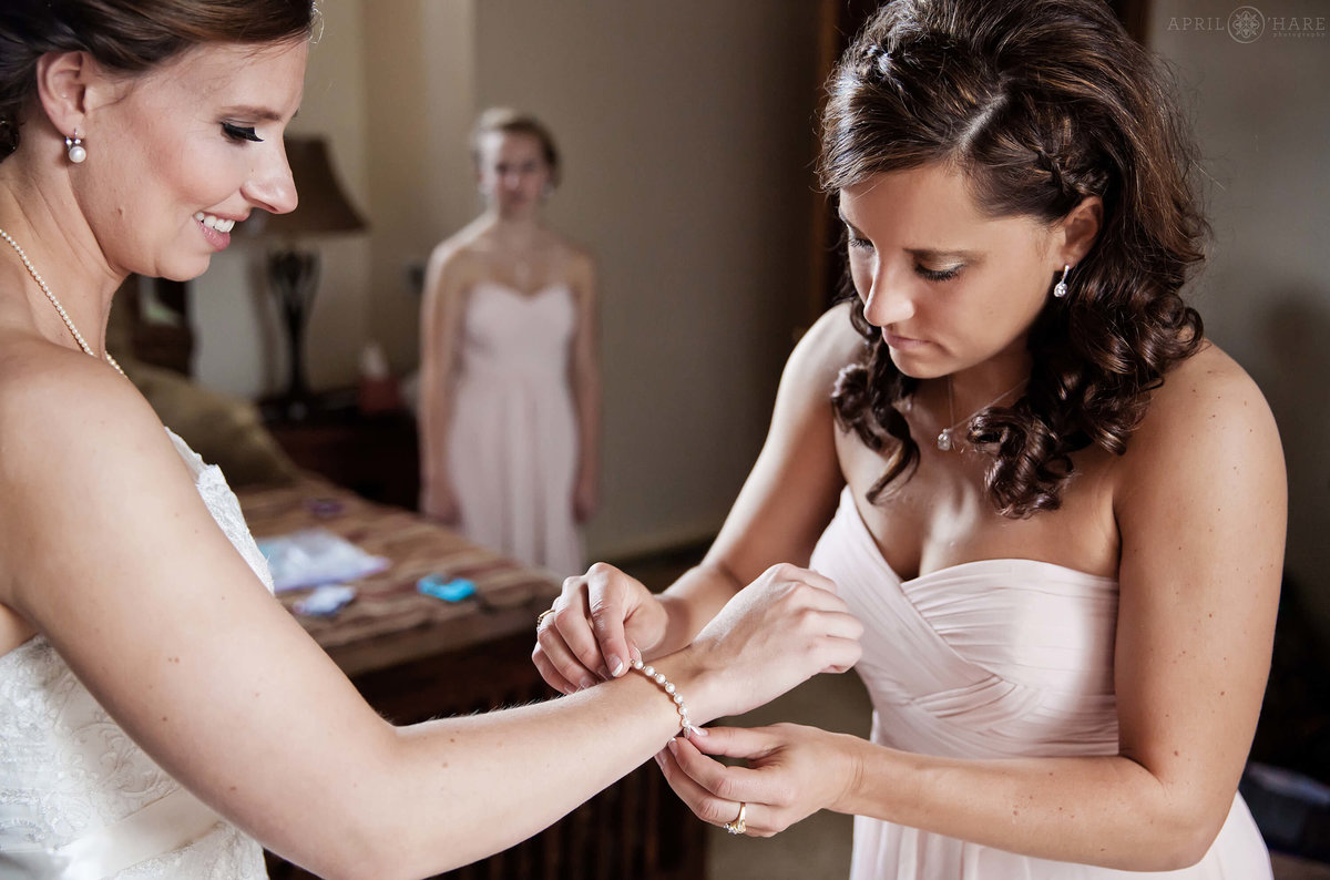 Bridesmaid helps bride with her bracelet jewelry at her Breckenridge Colorado wedding in the mountains