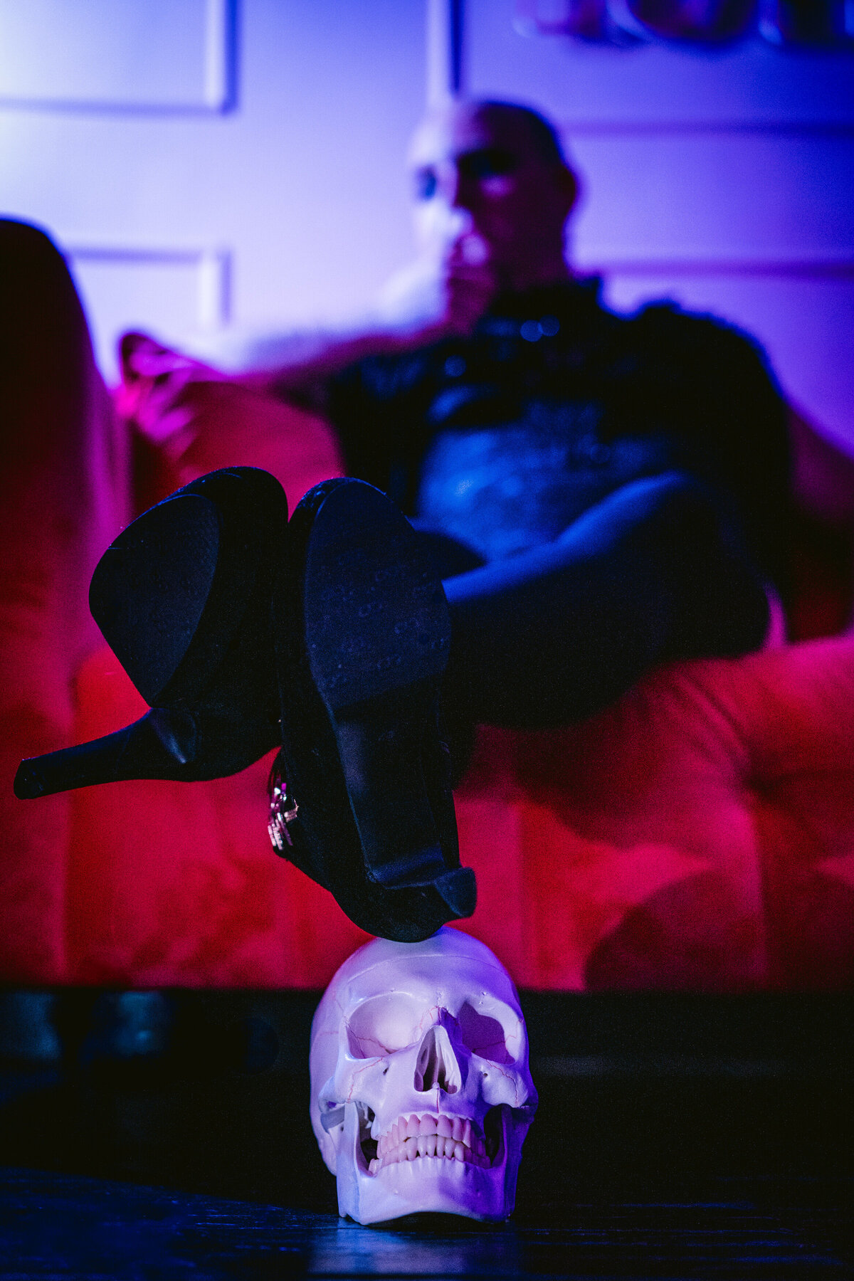 A person sitting on a couch resting their heels on a fake skull.