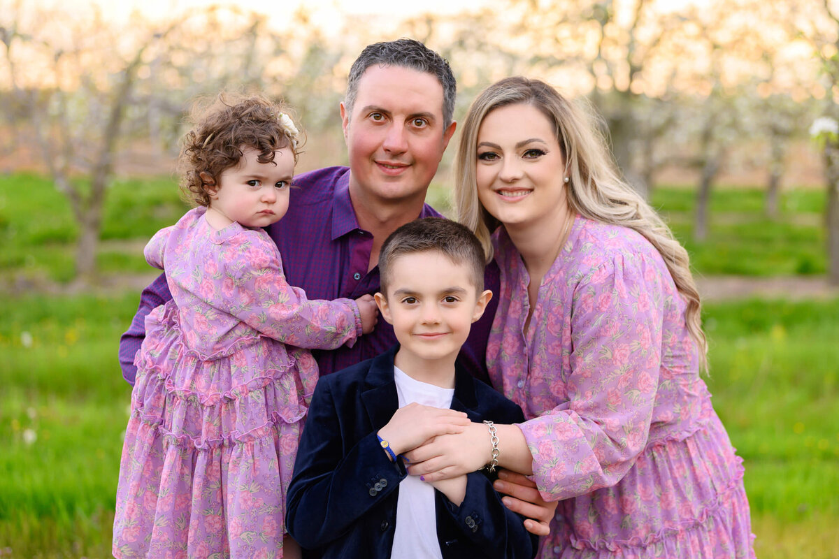 up close photo of mom and dad with their son and daughter wearing pink in the Golden Hour at the cherry blossom farm for their Spring family photos in Burlington, On