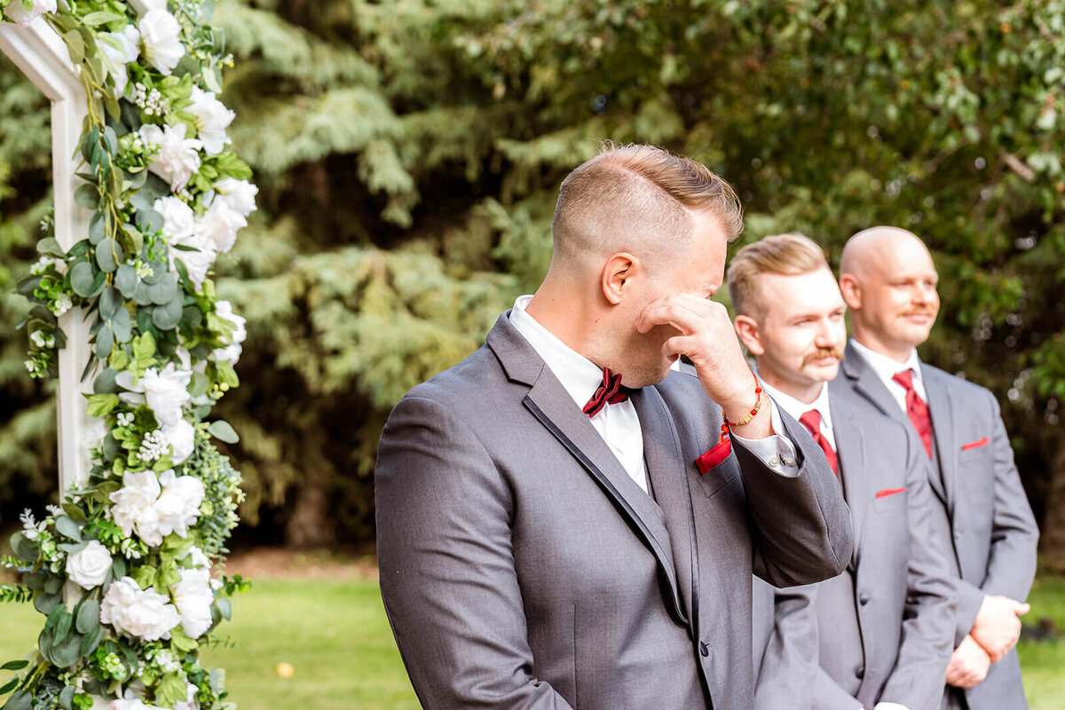 Groom wiping tear during first look while bride walks down aisle