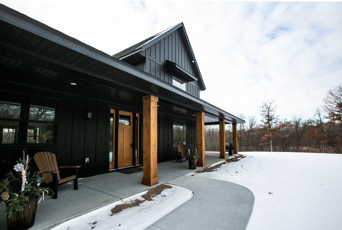 Exterior view of custom home in Elk River, Minnesota with black siding, wood details and front porch built by Cornerstone Custom Builds