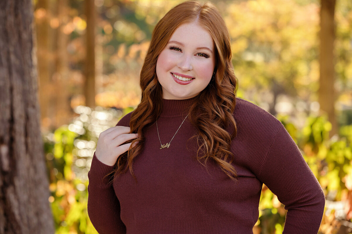 Sweet high school senior portrait  in a cranberry top with beautiful fall foliage in the background