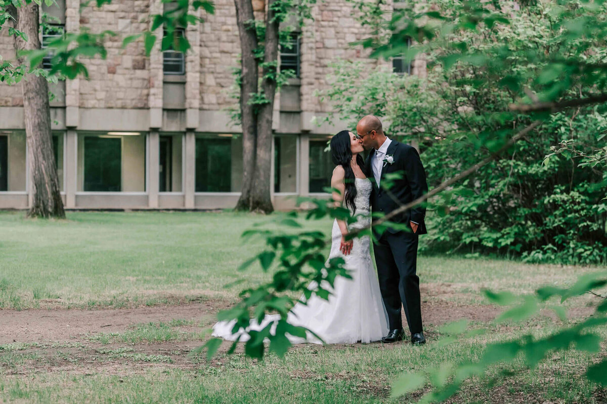 A bride and groom are sharing a kiss  while on the university grounds.