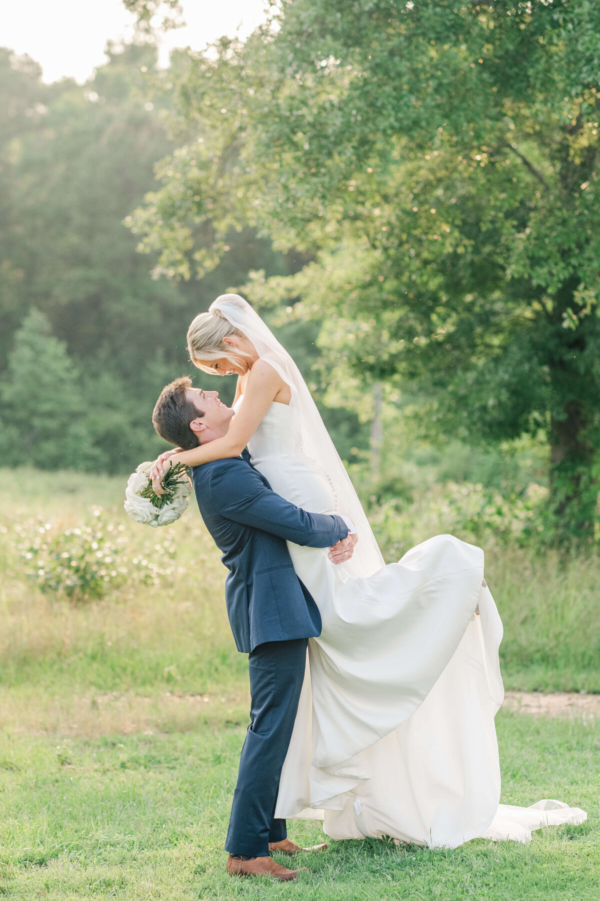 Alabama groom lifting bride up in a field while staring into each others eyes