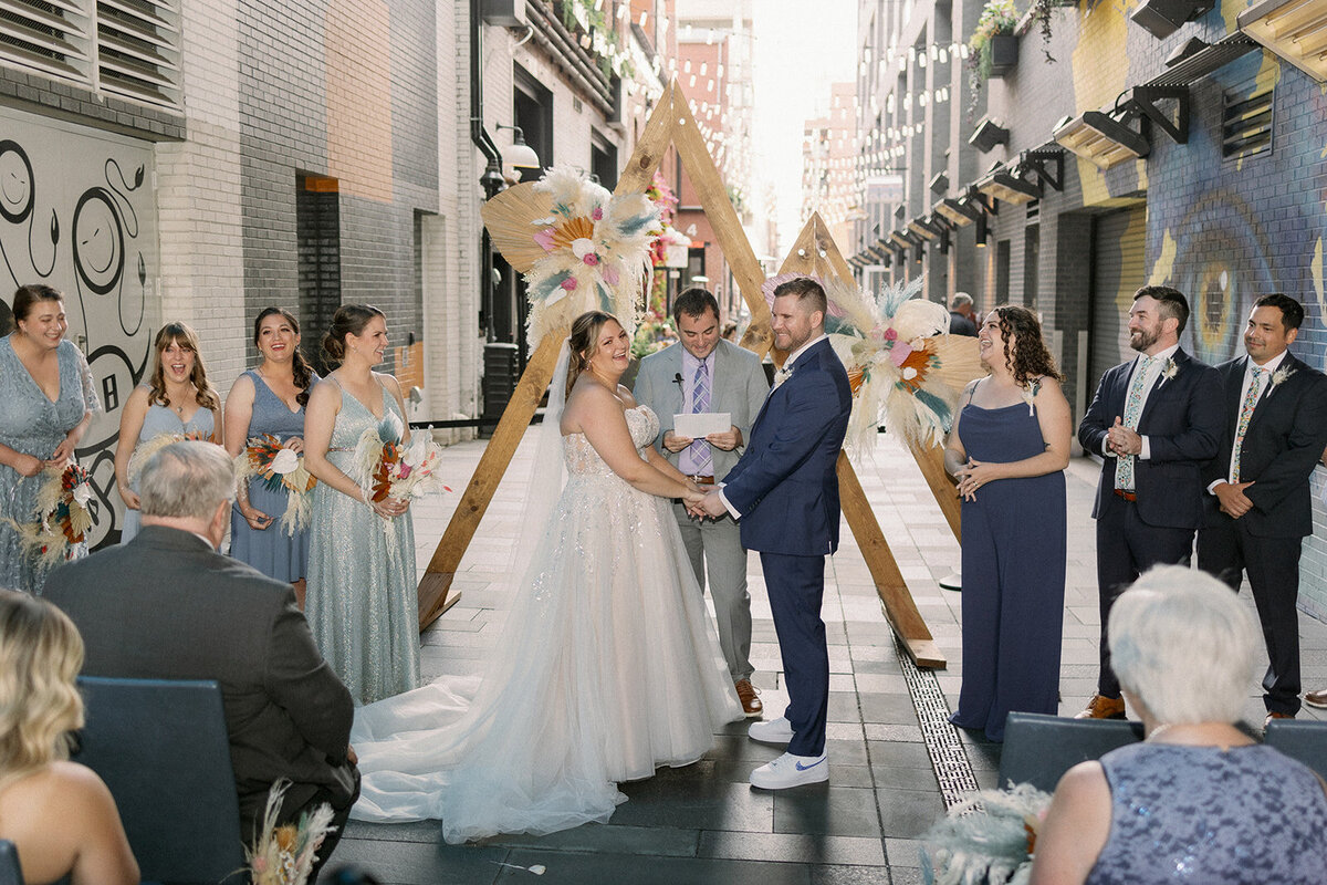Bride and groom get married in the Dairy Block Alley in Denver Colorado in front of a triangle arch.