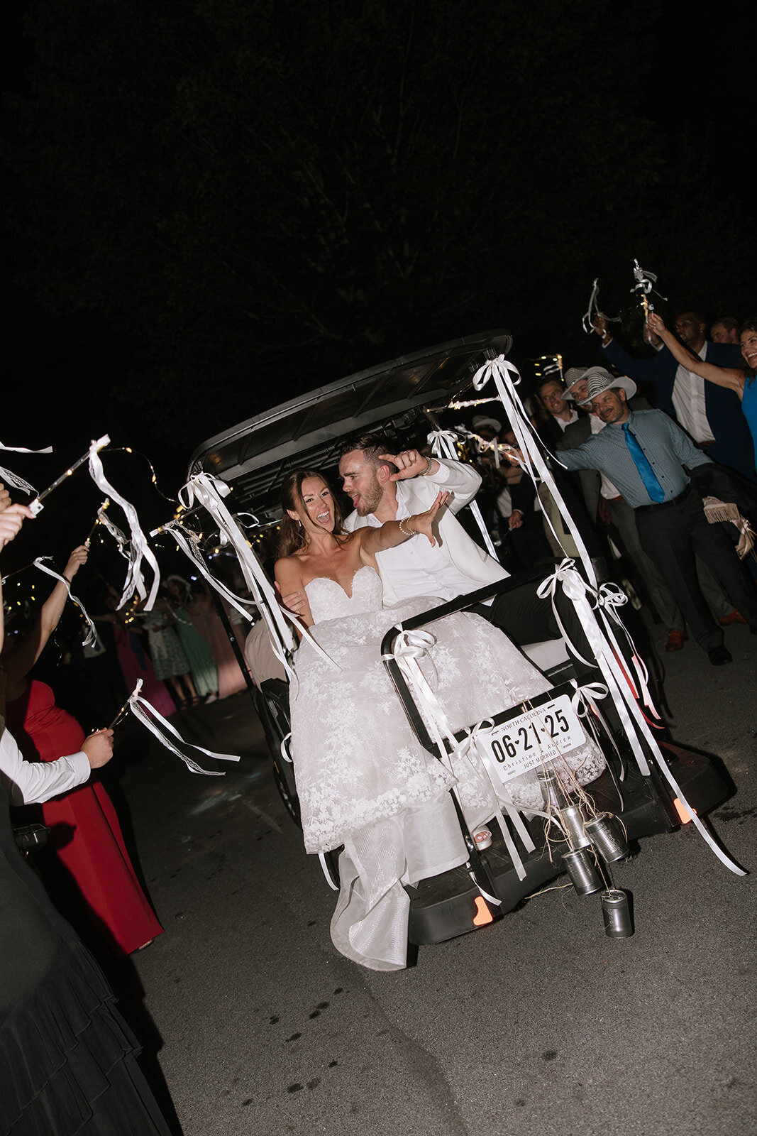 Bride and groom exit their wedding reception in a decorated golf cart while guests cheer at Trillium Links in Cashiers, NC.