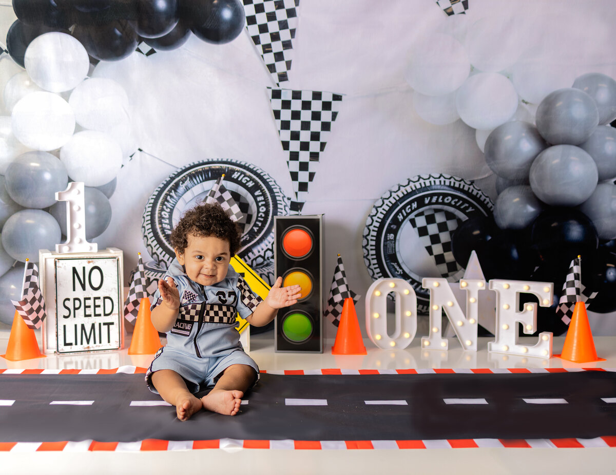 Race car themed first birthday cake smash with baby boy in racing outfit, checkered flags, and road setup in Waldwick NJ studio