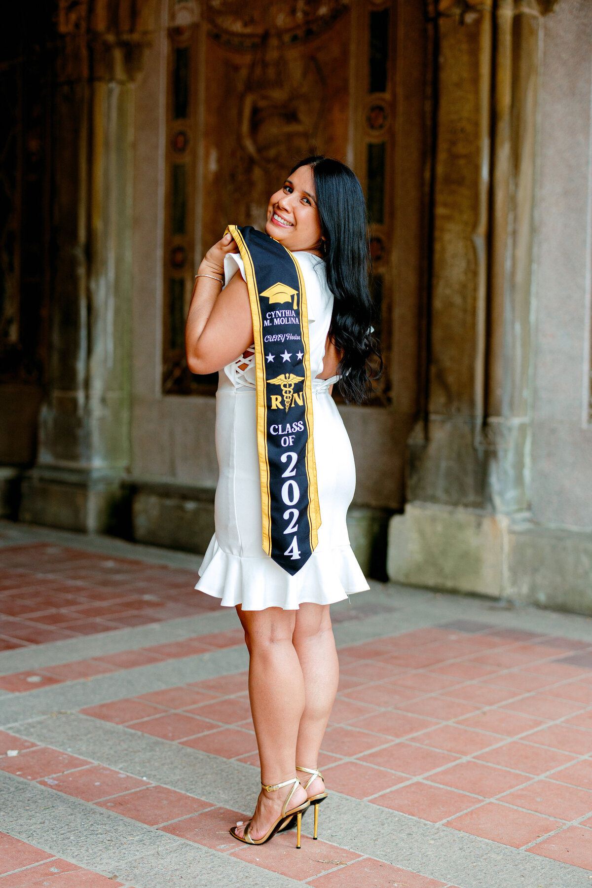 Hostos Community College nursing graduate smiling while holding stole at Central Park.