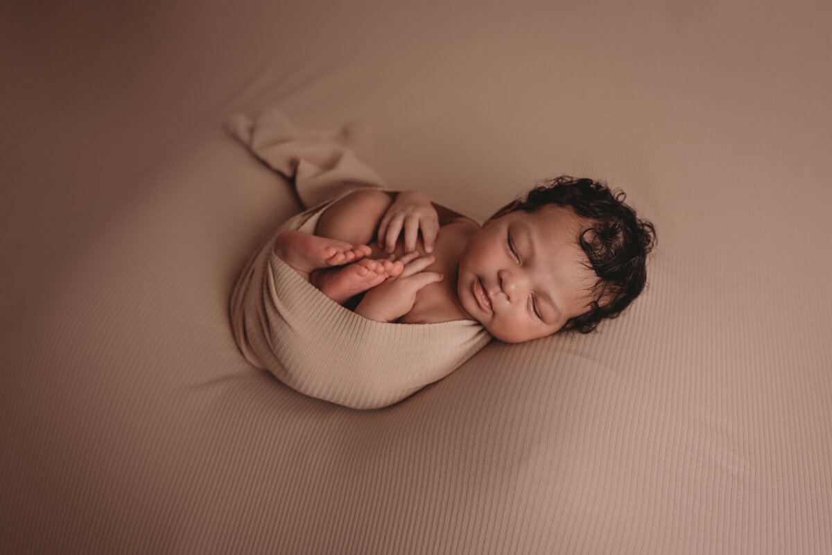 newborn photo session at atlanta newborn photography studio with baby girl asleep on back wrapped up in pale pink fabric on pale pink backdrop